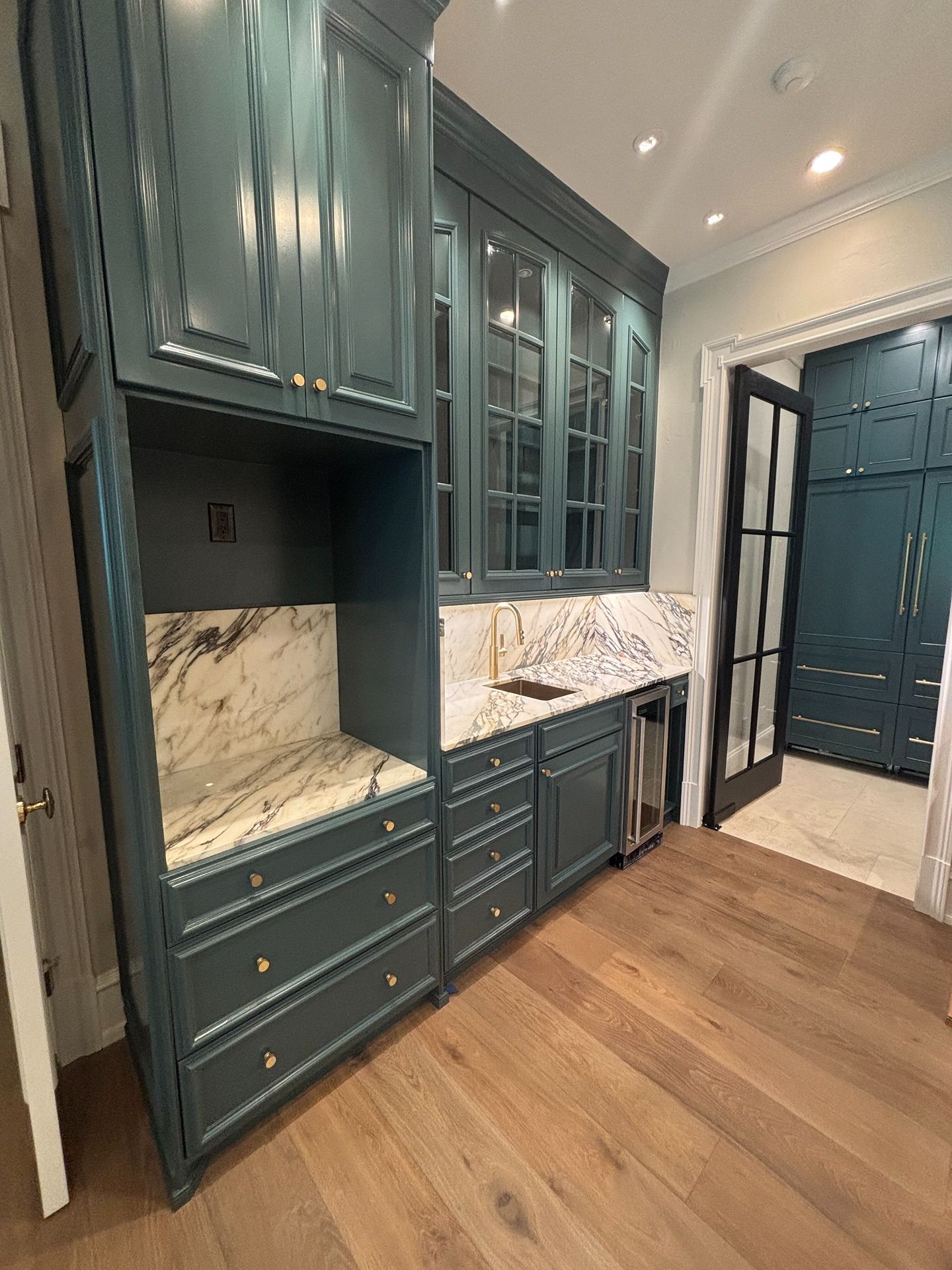 A kitchen area featuring dark blue cabinetry, marble countertops, and light wood flooring, with a visible wine fridge.