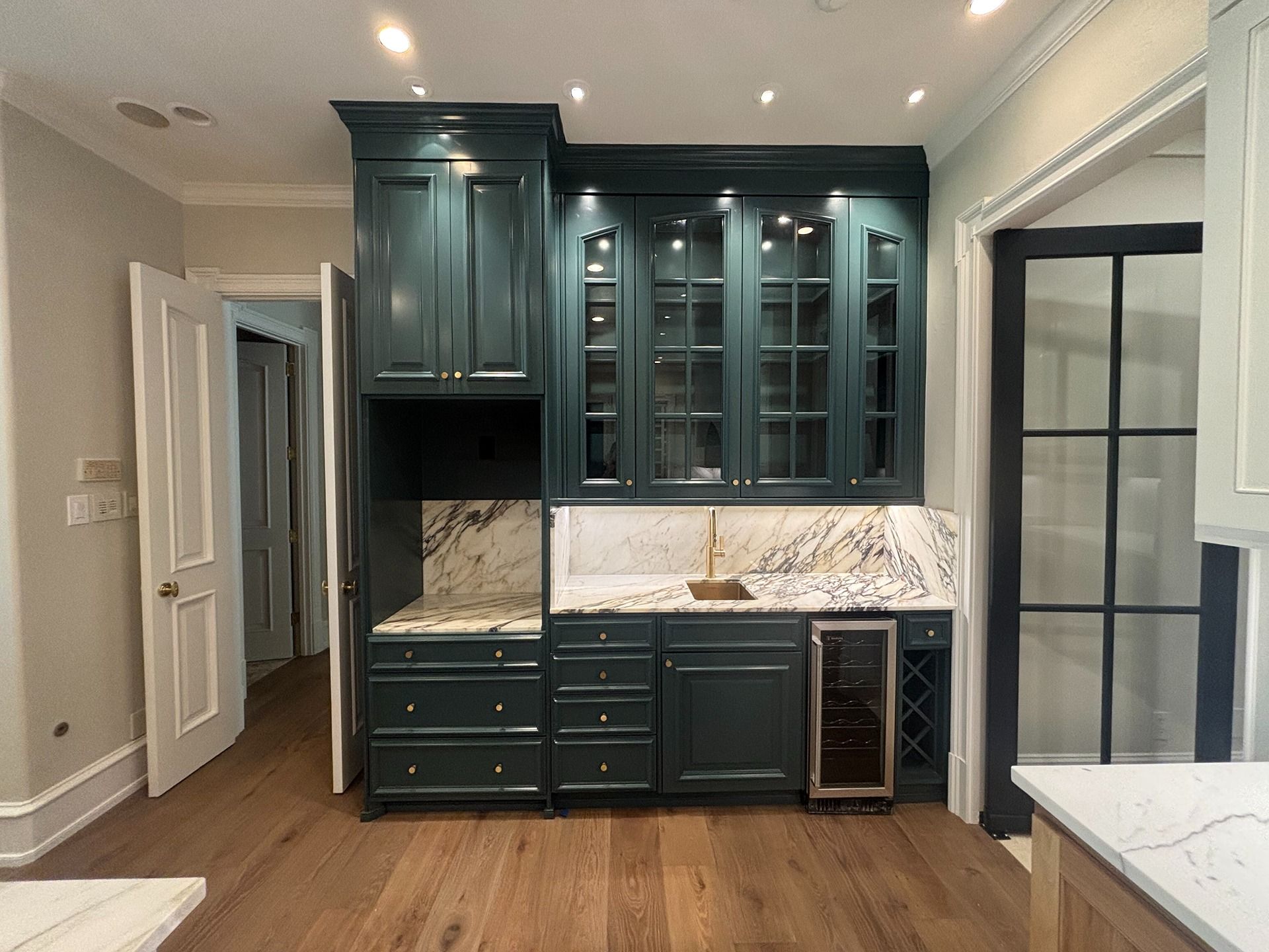 Dark green kitchen cabinetry featuring glass-front cabinets, a marble countertop, small sink, and a wine cooler.