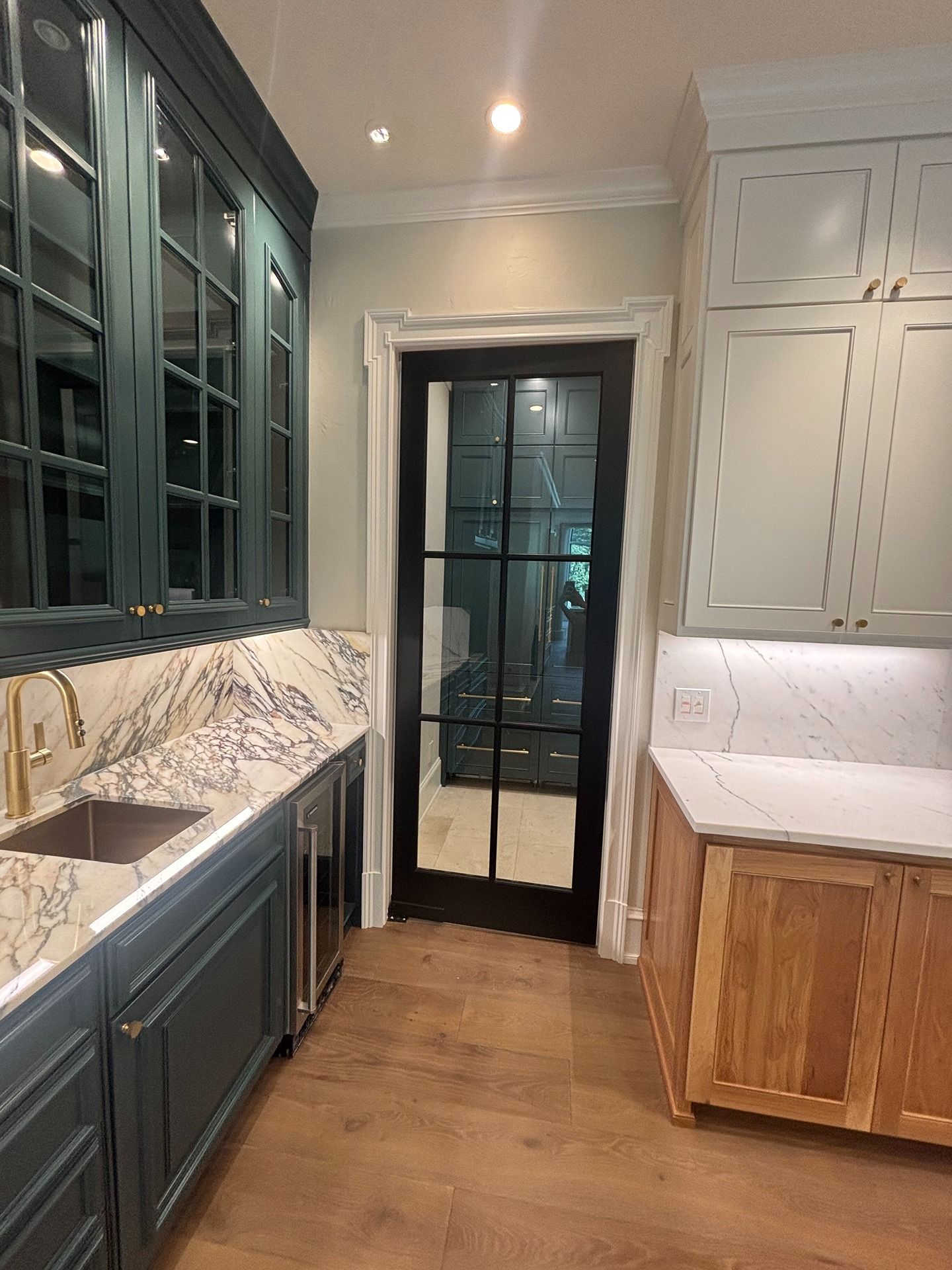 Kitchen with teal cabinets, wood-toned base cabinets, white marble countertops, and a black-framed glass door.