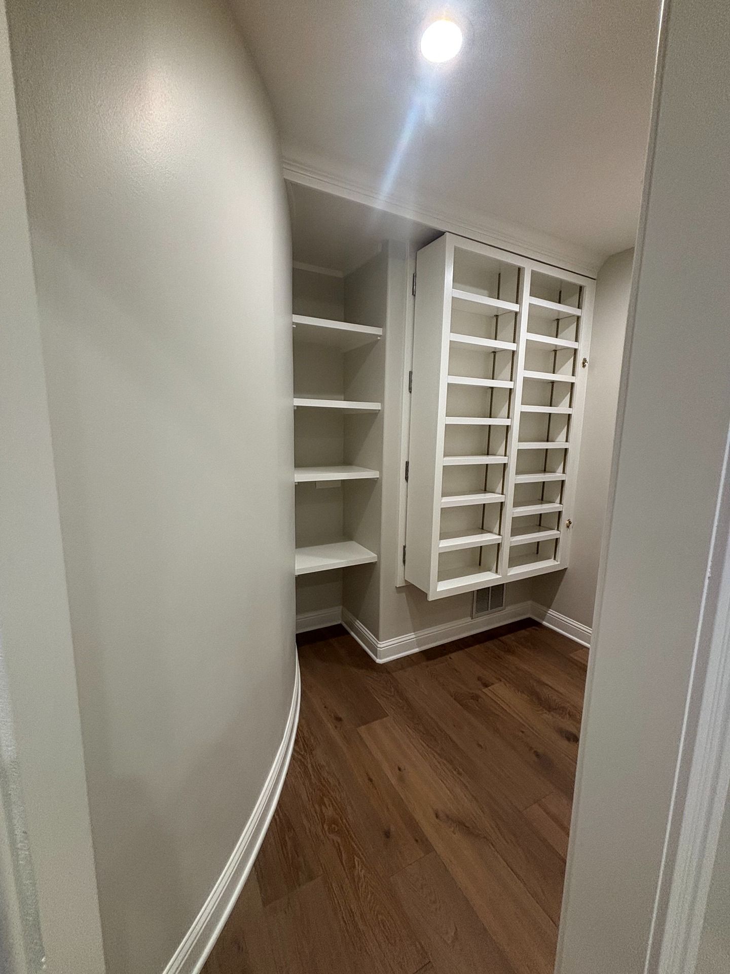 A hallway with curved cream walls, wood flooring, and built-in white shelving units.