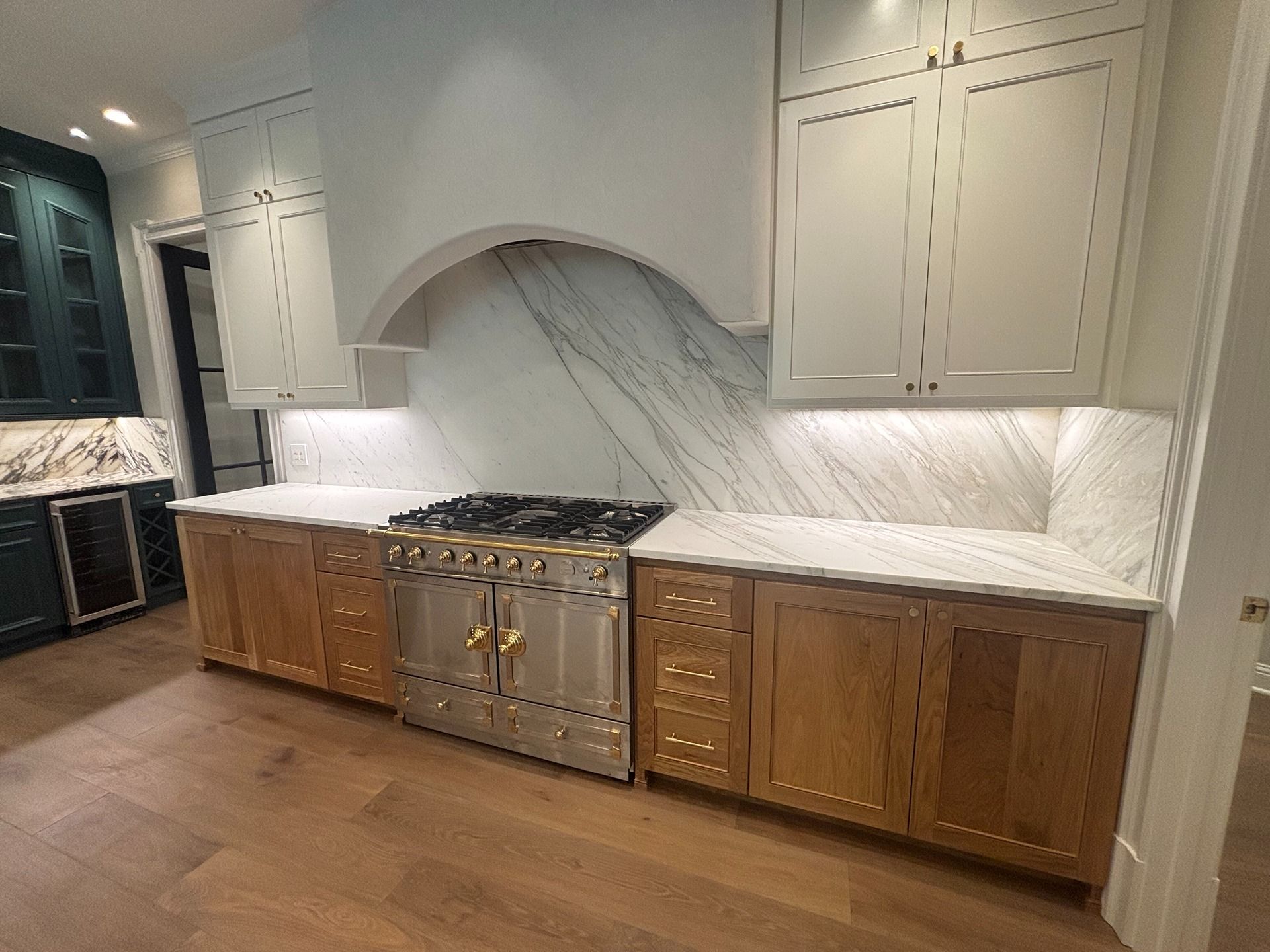 A kitchen with oak cabinets, a large stainless steel range, a marble backsplash, and white upper cabinets.