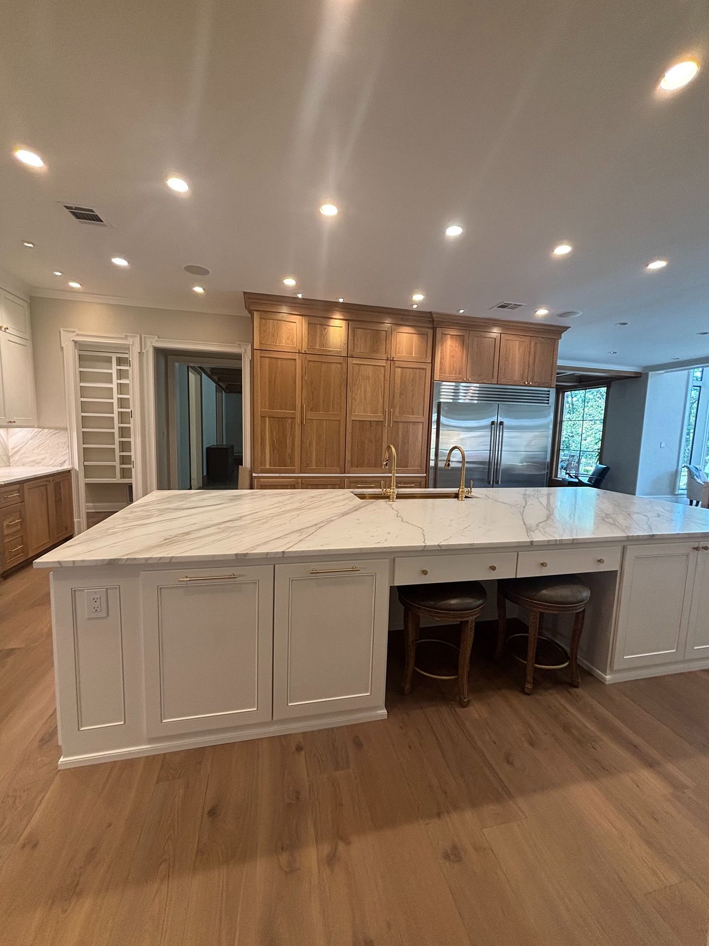A kitchen island with a white marble countertop, cream cabinets, and stools, with tall wooden cabinets in the background.