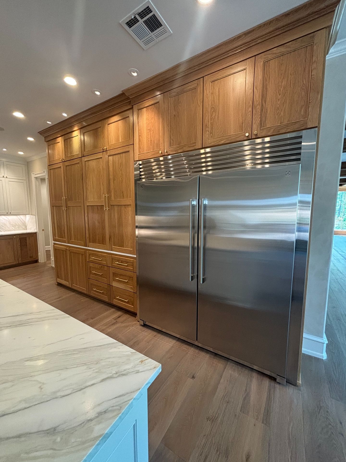 A stainless steel, side-by-side refrigerator built into a wall of oak cabinetry with marble countertops in a kitchen.