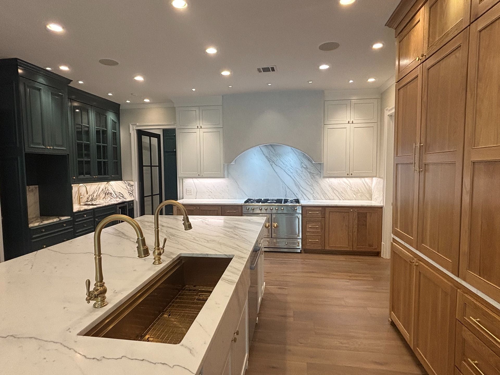 A spacious, modern kitchen with a large marble island, gold-toned farmhouse sink, and a mix of dark and wood-toned cabinets.