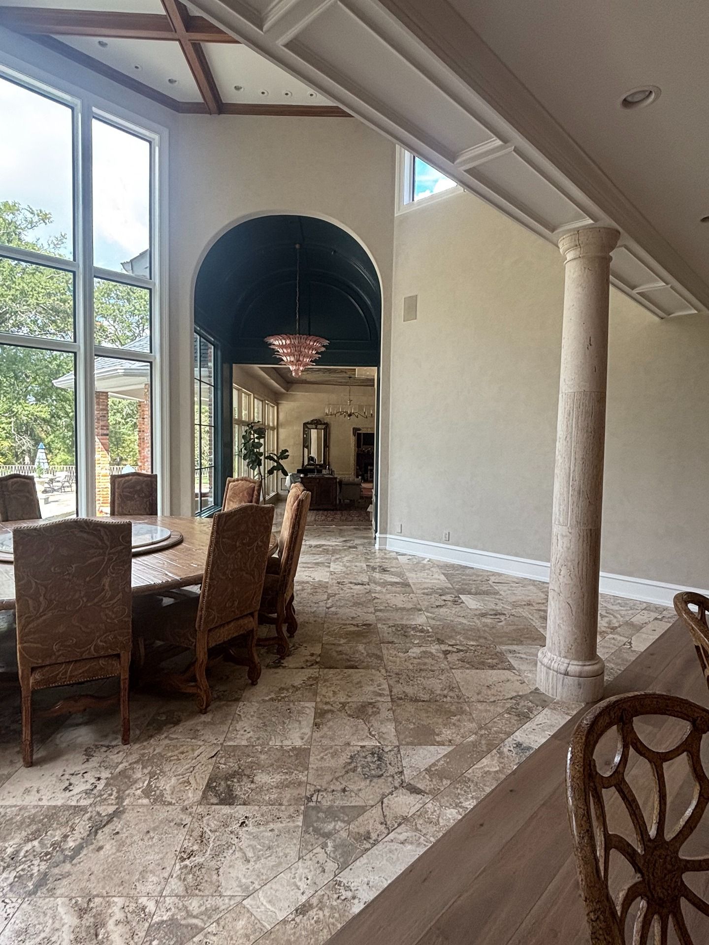 A dining area with a round table, stone tile flooring, and a decorative column, leading to a dark arched hallway.