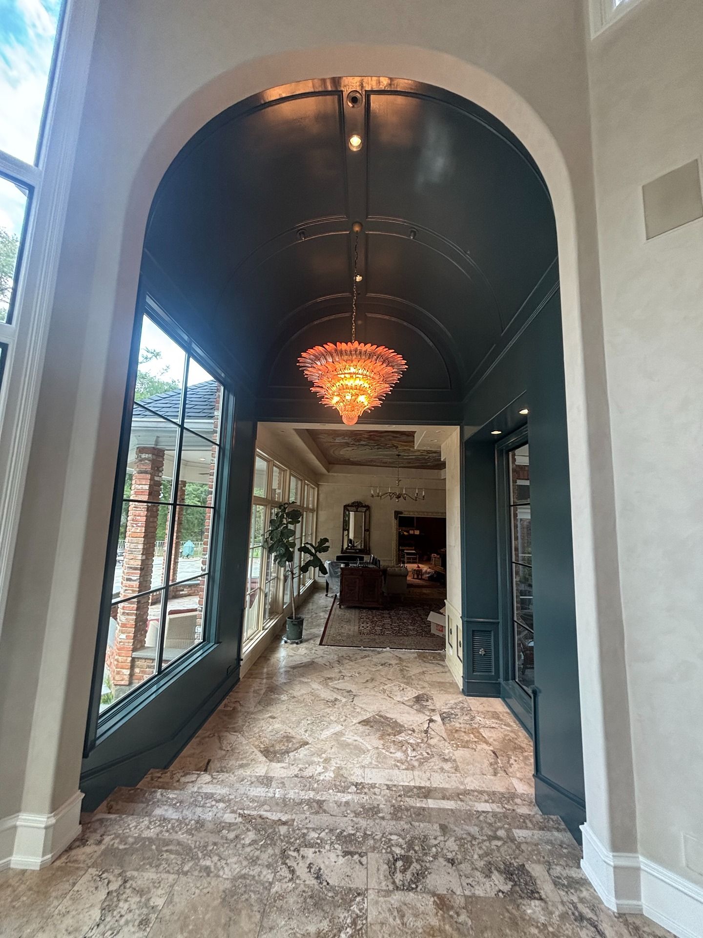A marble-floored hallway features a dark green arched ceiling, a hanging crystal chandelier, and large window wall panes.
