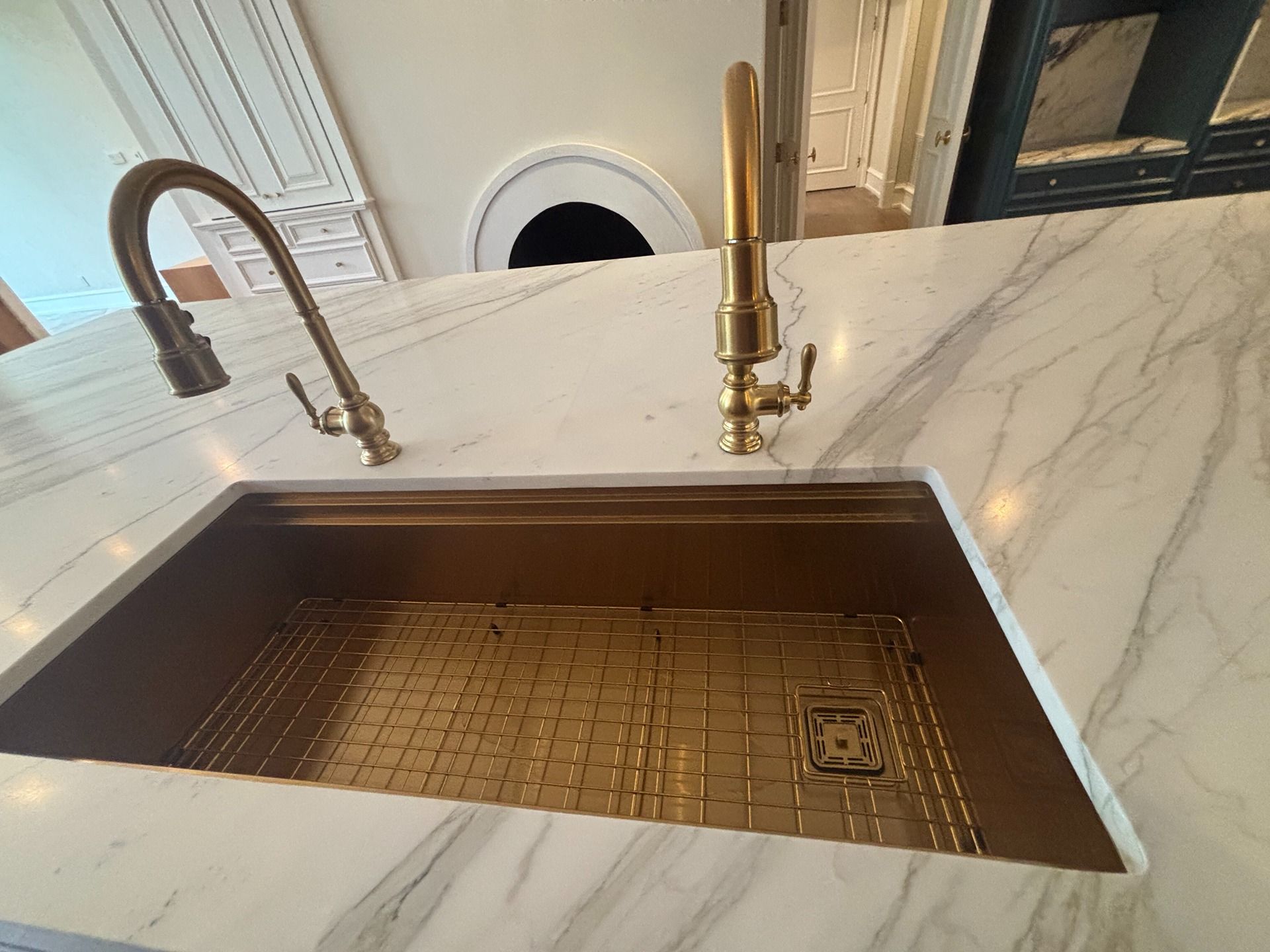 A gold-tone sink and two matching faucets are set into a white marble countertop with grey veining.