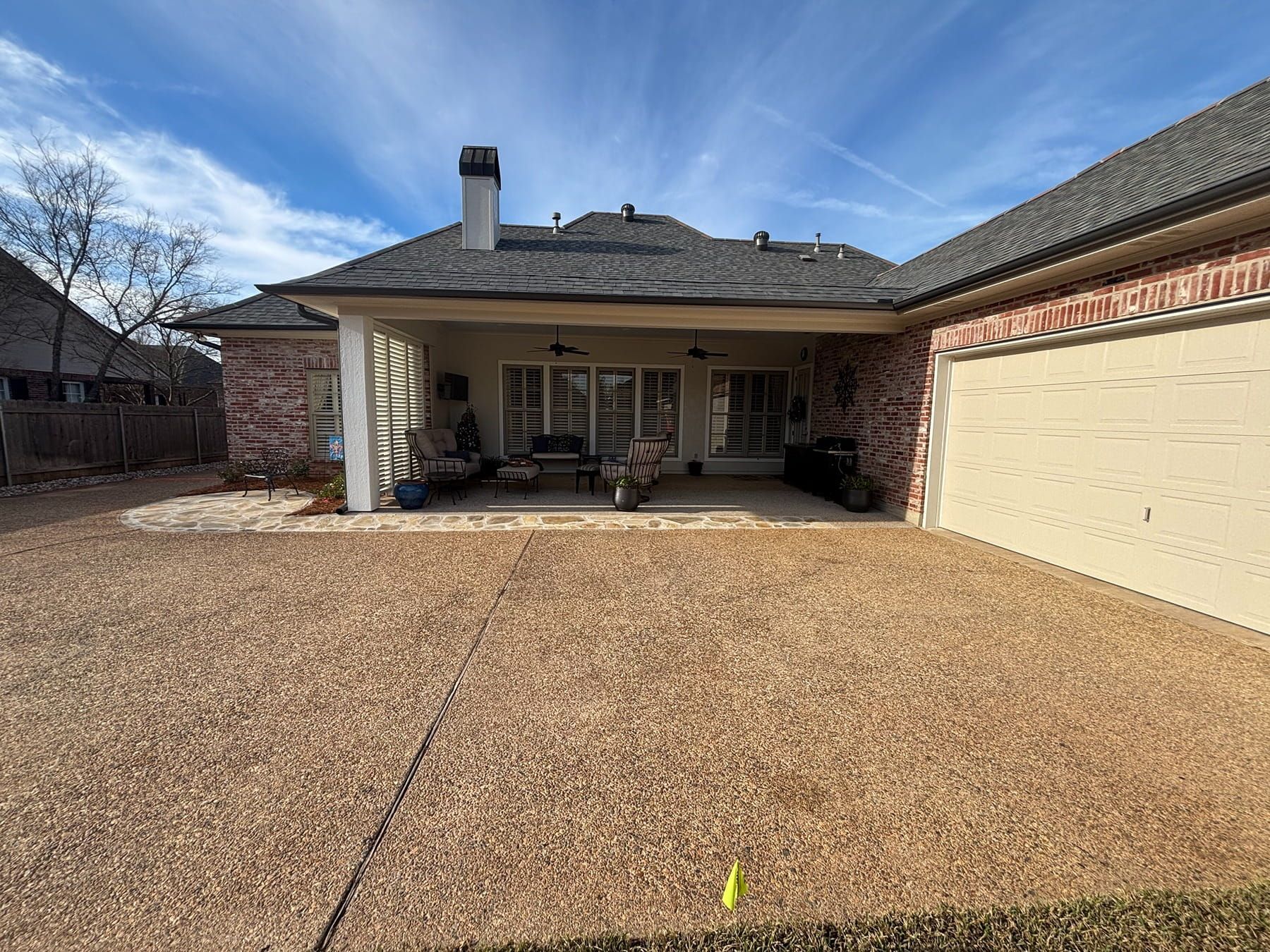 A backyard with a covered patio, brick and stucco house, attached garage, and a large gravel ground covering.
