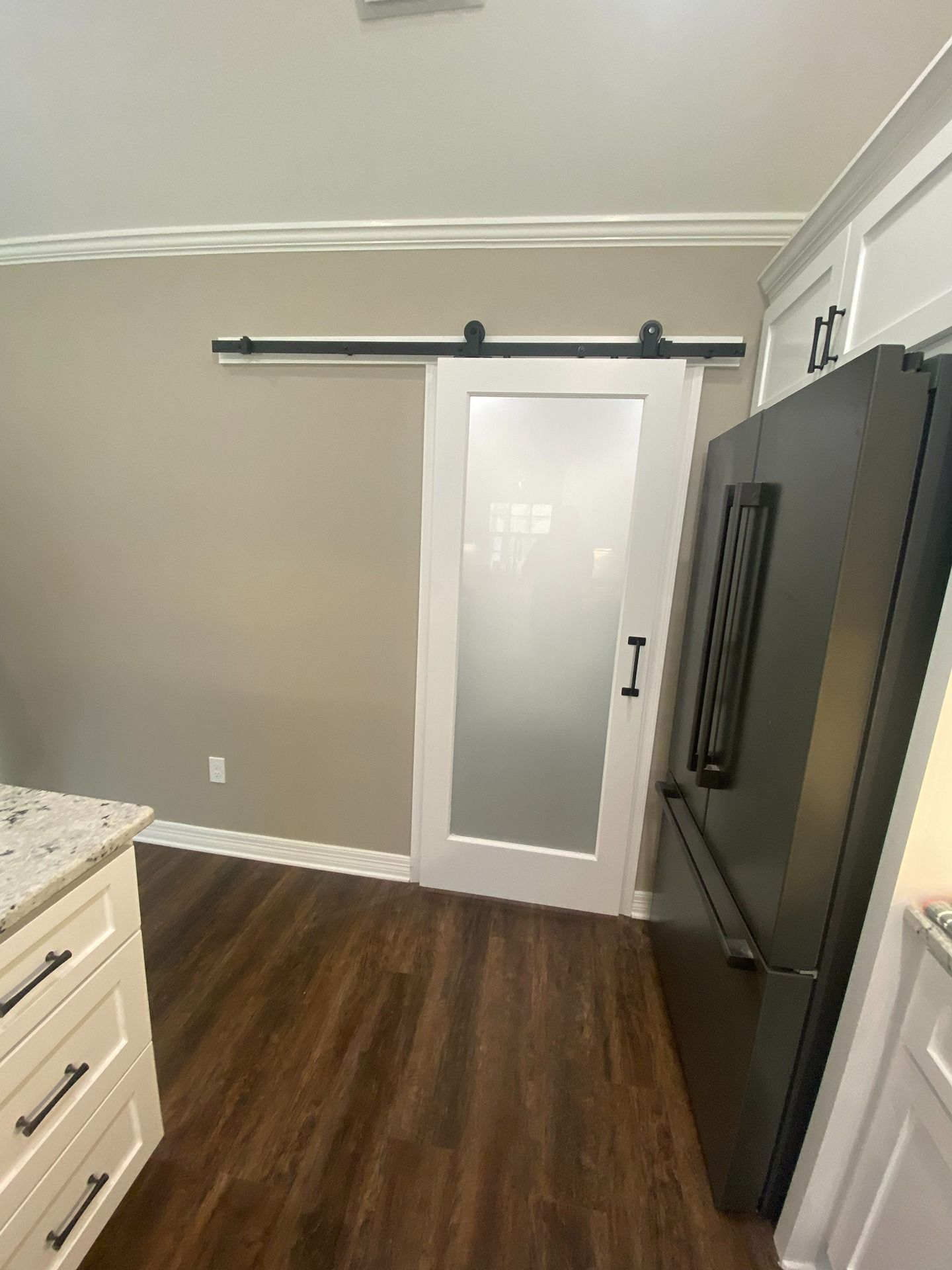 White frosted glass sliding barn door in a room with light grey walls, dark wood floors, and a black refrigerator.
