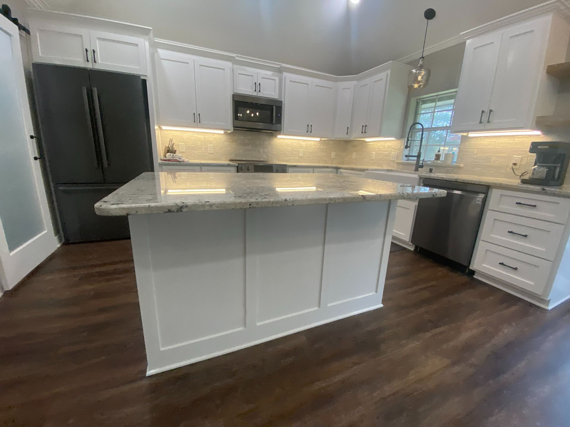 Modern kitchen with white cabinetry, granite island countertop, stainless steel appliances, and dark wood flooring.