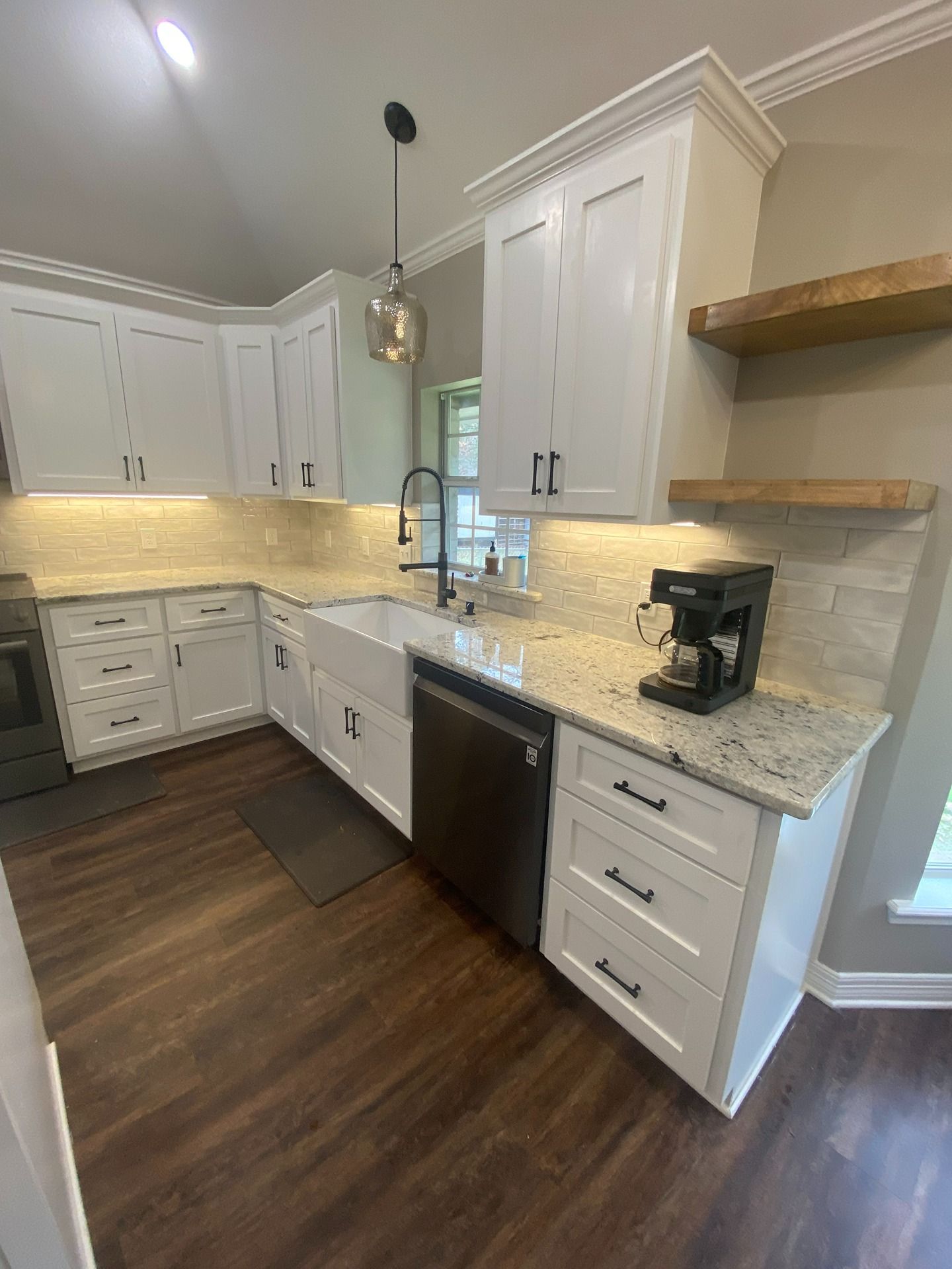 A bright kitchen with white cabinets, light granite countertops, a farmhouse sink, stainless appliances, and wood floors.