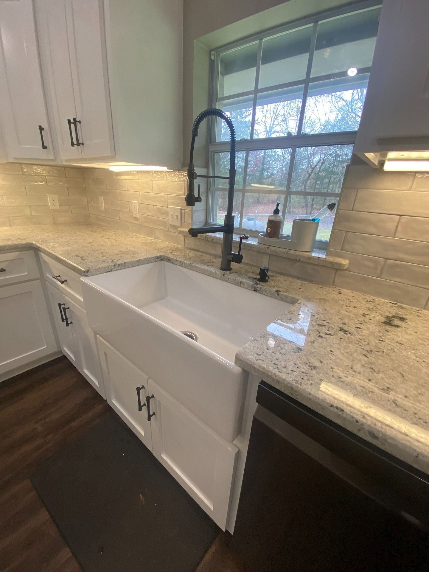 A bright kitchen featuring a white farmhouse sink, speckled granite countertops, white cabinetry, and a dark faucet.