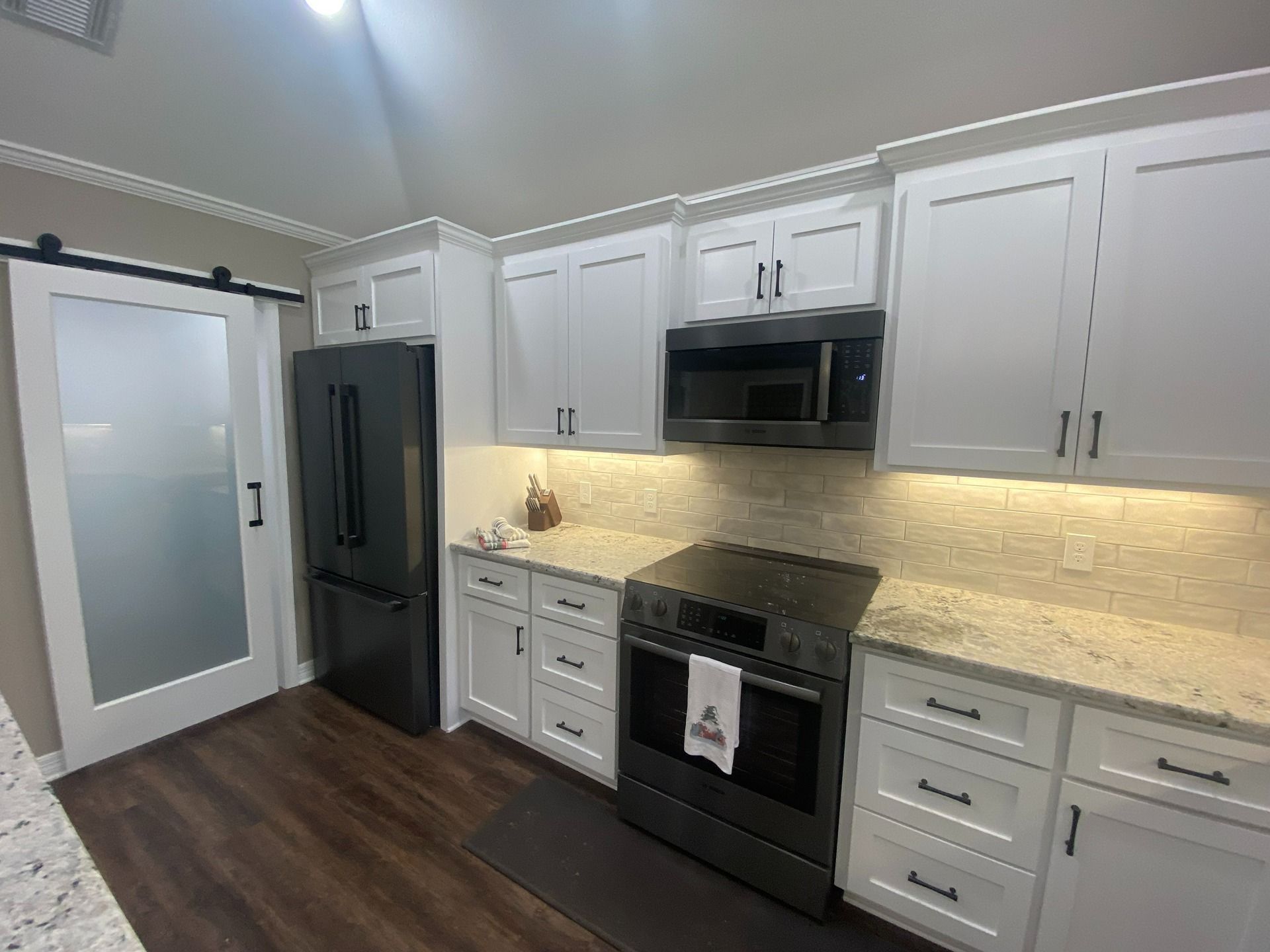 A modern kitchen with white cabinets, speckled granite countertops, a dark refrigerator, and a frosted glass sliding door.