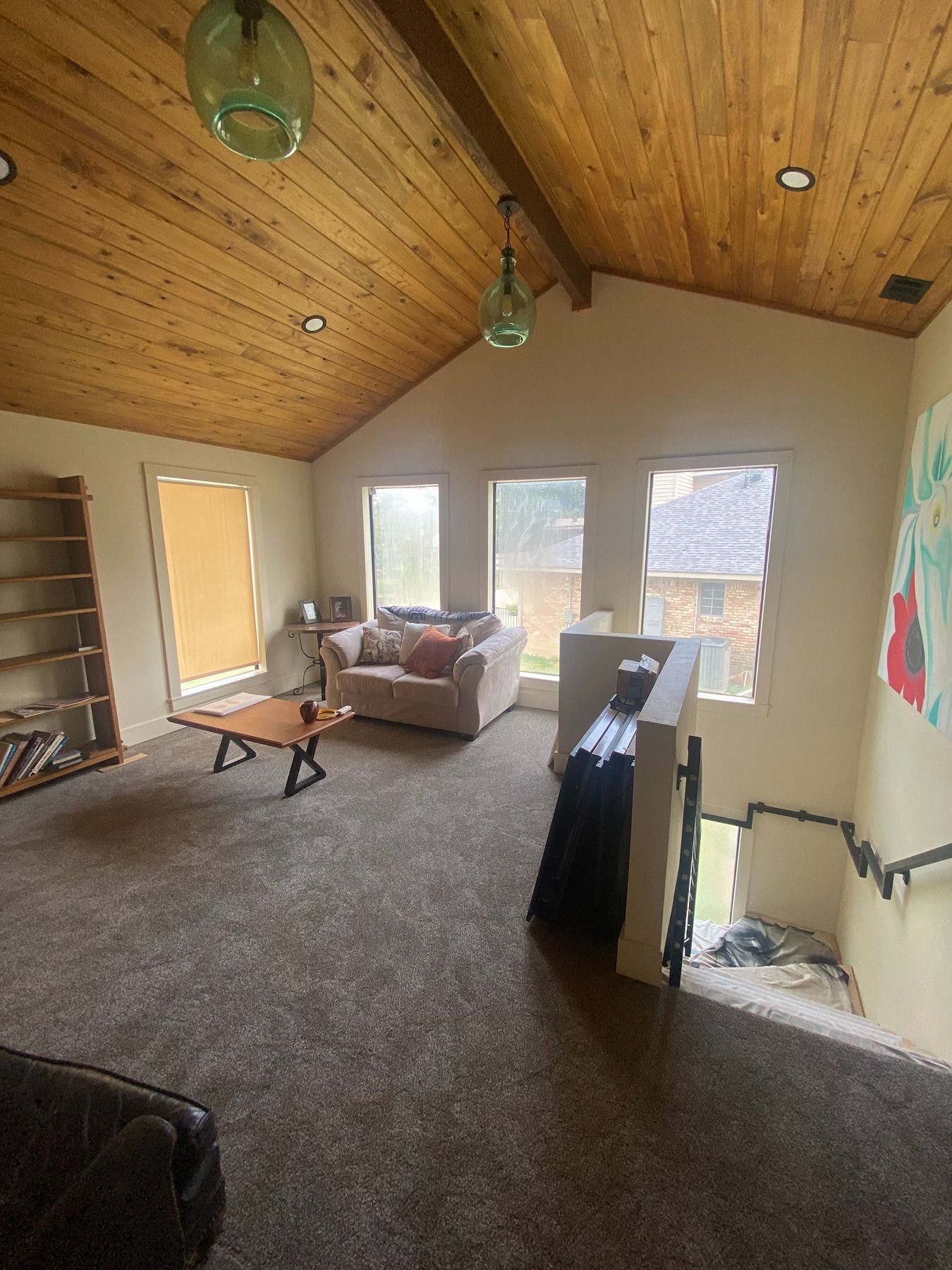 A spacious loft room with a wooden vaulted ceiling, tan walls, a gray carpet, a small seating area, and a staircase.