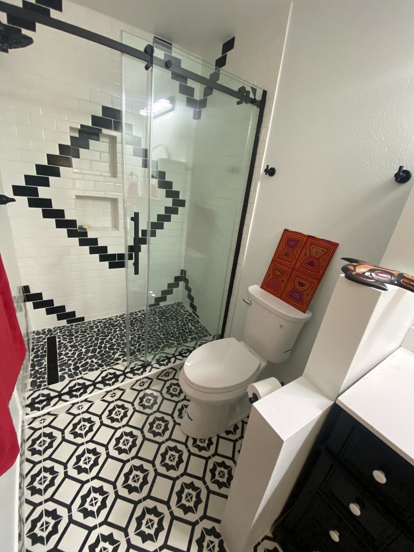 A modern bathroom featuring a patterned tile floor, a glass-enclosed shower with a black diamond tile design, and a toilet.