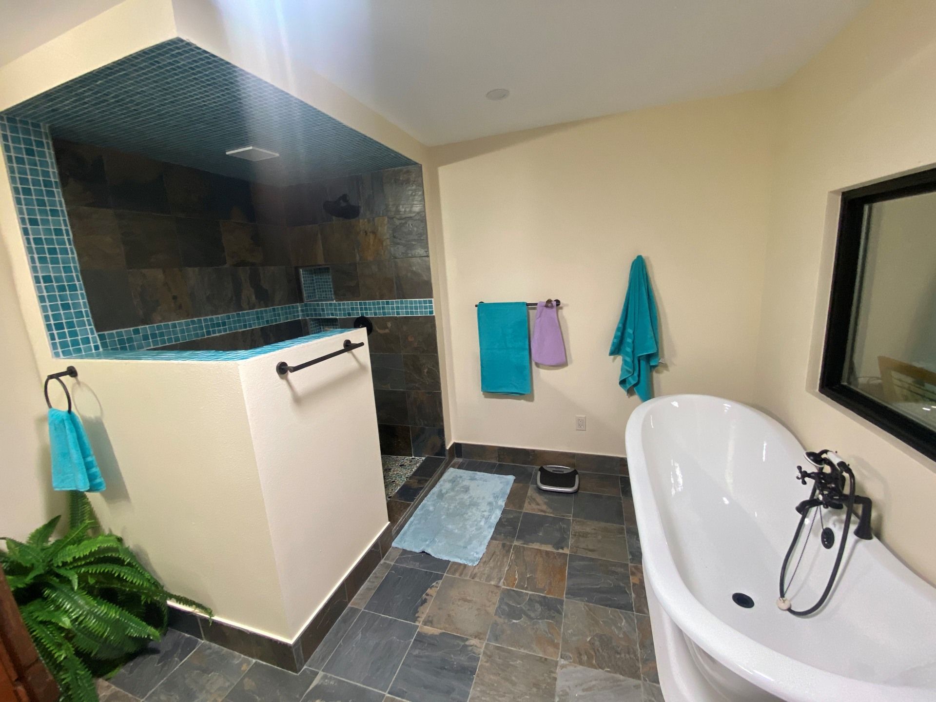 A bathroom featuring a walk-in slate shower with blue mosaic tiles, a freestanding white tub, and slate floor tiles.