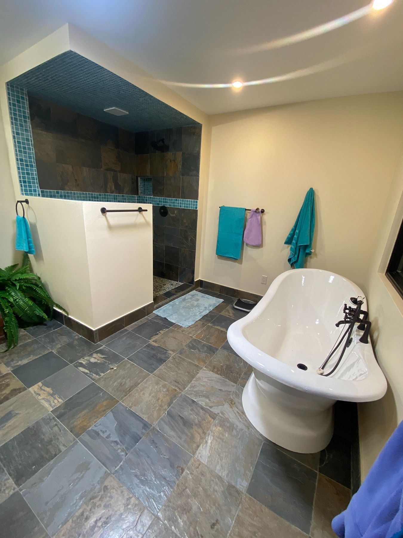 A spacious bathroom featuring a slate tile floor, a walk-in shower with turquoise accent tiles, and a white soaking tub.