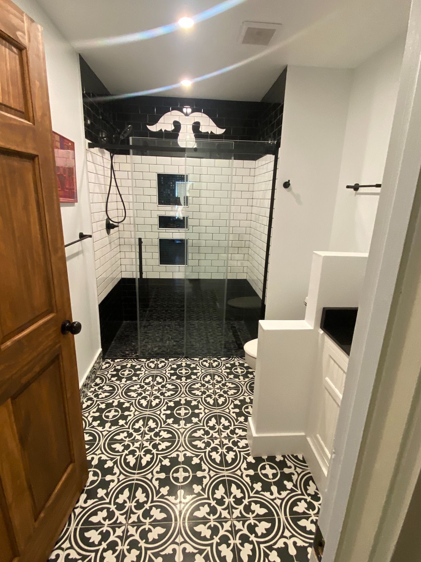 A bathroom with black and white patterned tile flooring, a glass-enclosed shower with white subway tiles, and a vanity.