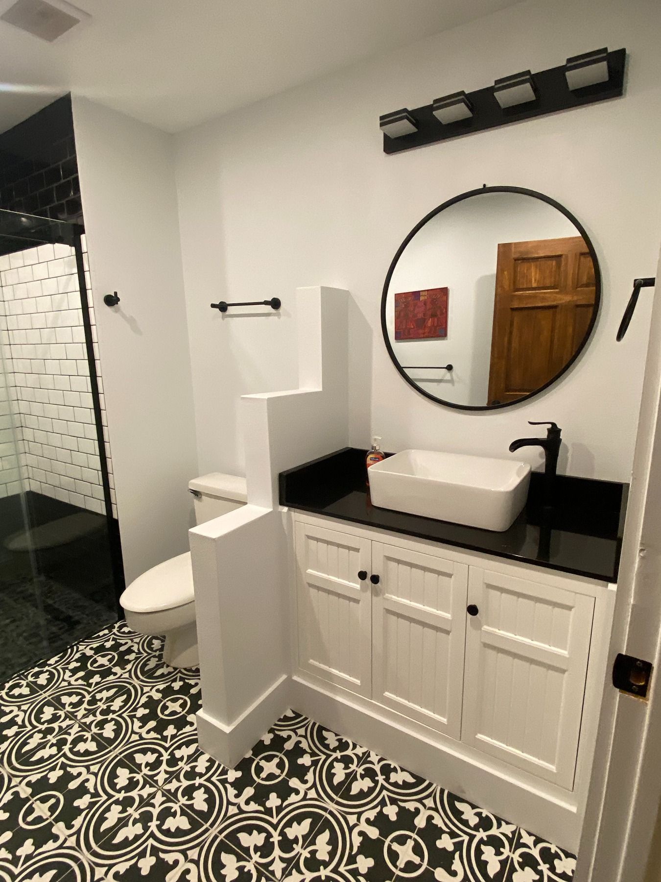 A bathroom featuring black and white patterned tile flooring, a white vanity with a black countertop, and a round mirror.