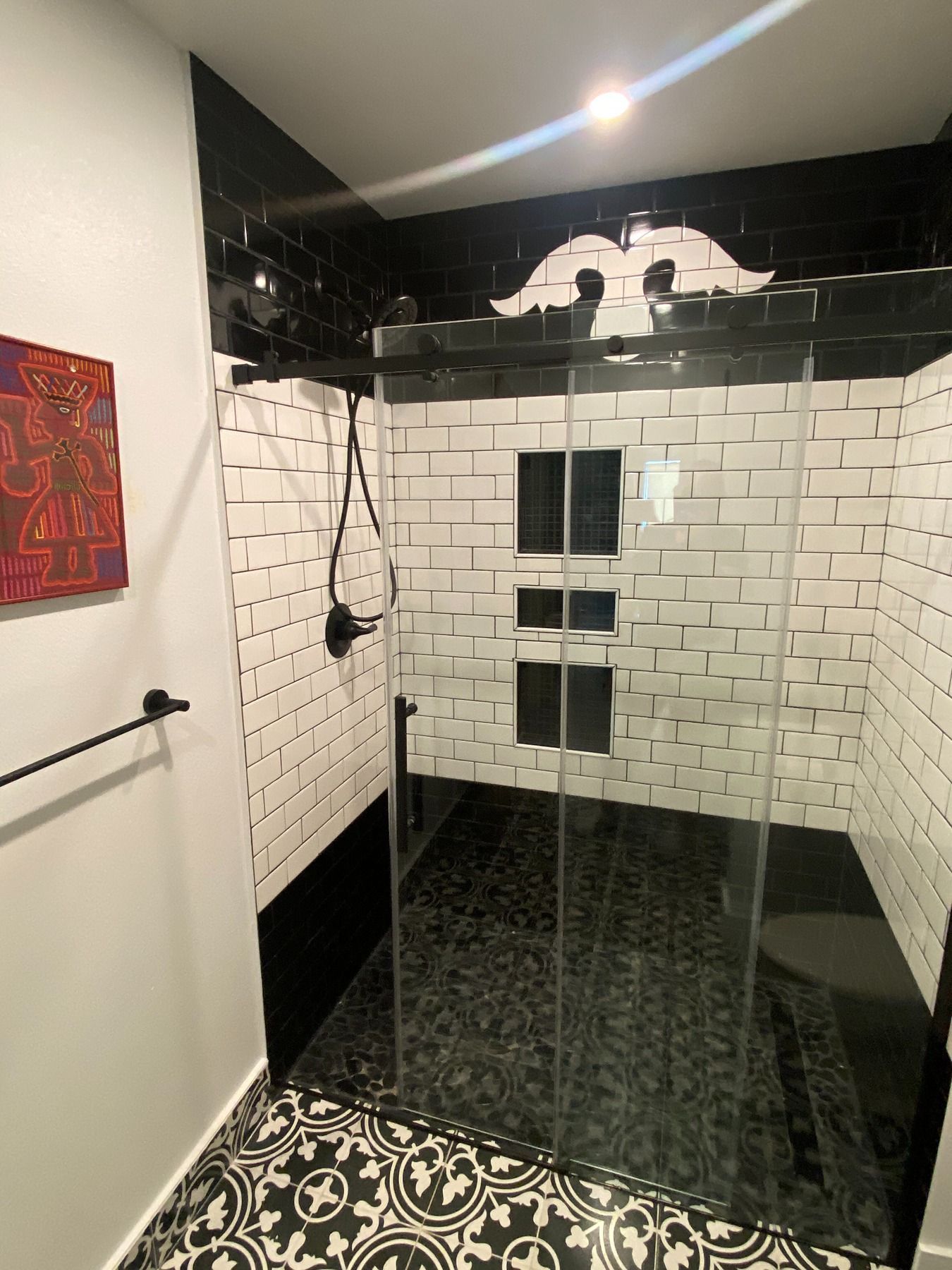A modern bathroom shower with white brick-style walls, black tile accents, and patterned black and white floor tiles.