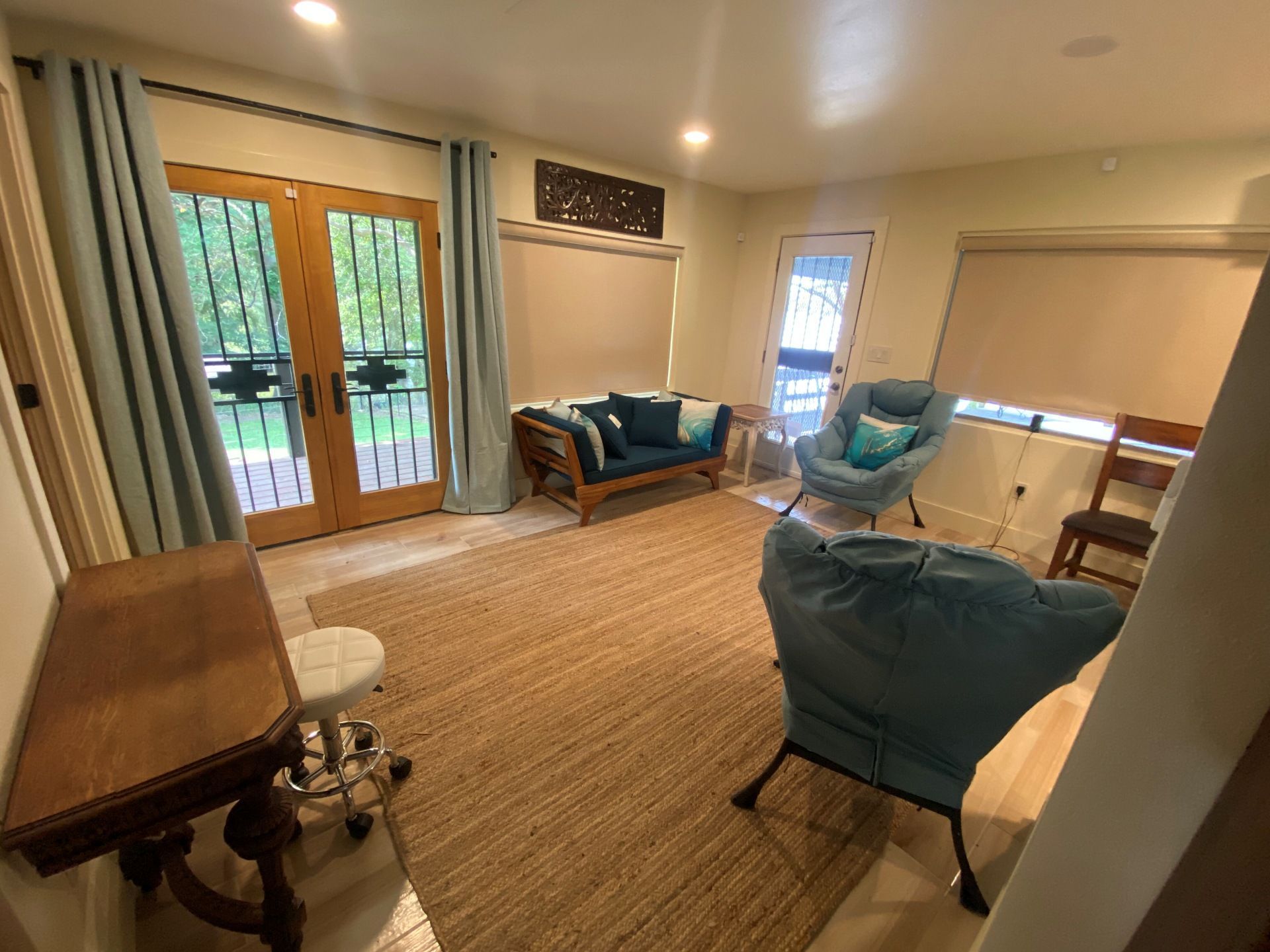 Living room with a wooden table, rug, blue couch, two teal armchairs, and glass doors with light blue curtains.