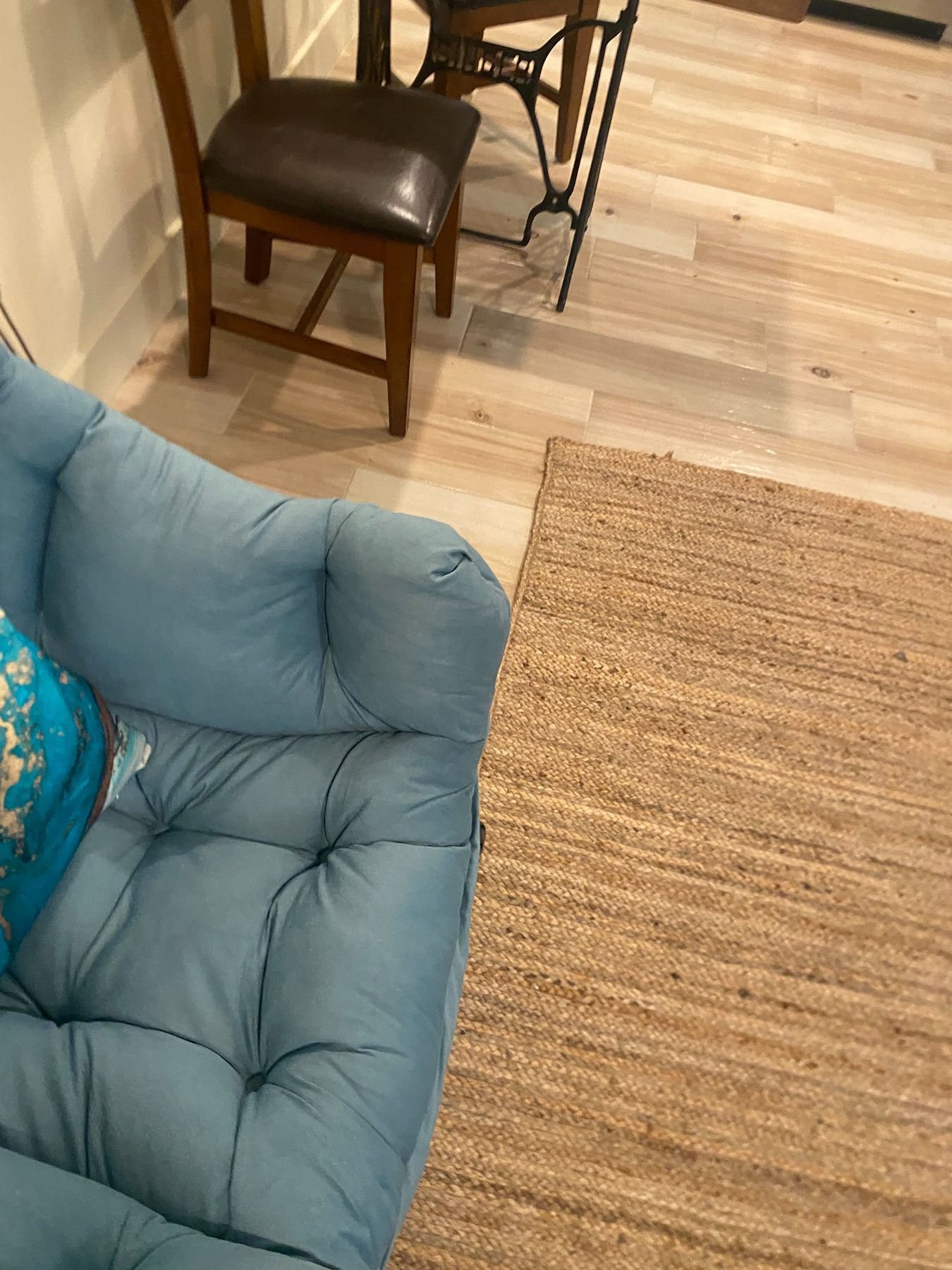 A blue tufted couch sits next to a woven rug, with a wooden dining chair and a vintage table base in the background.