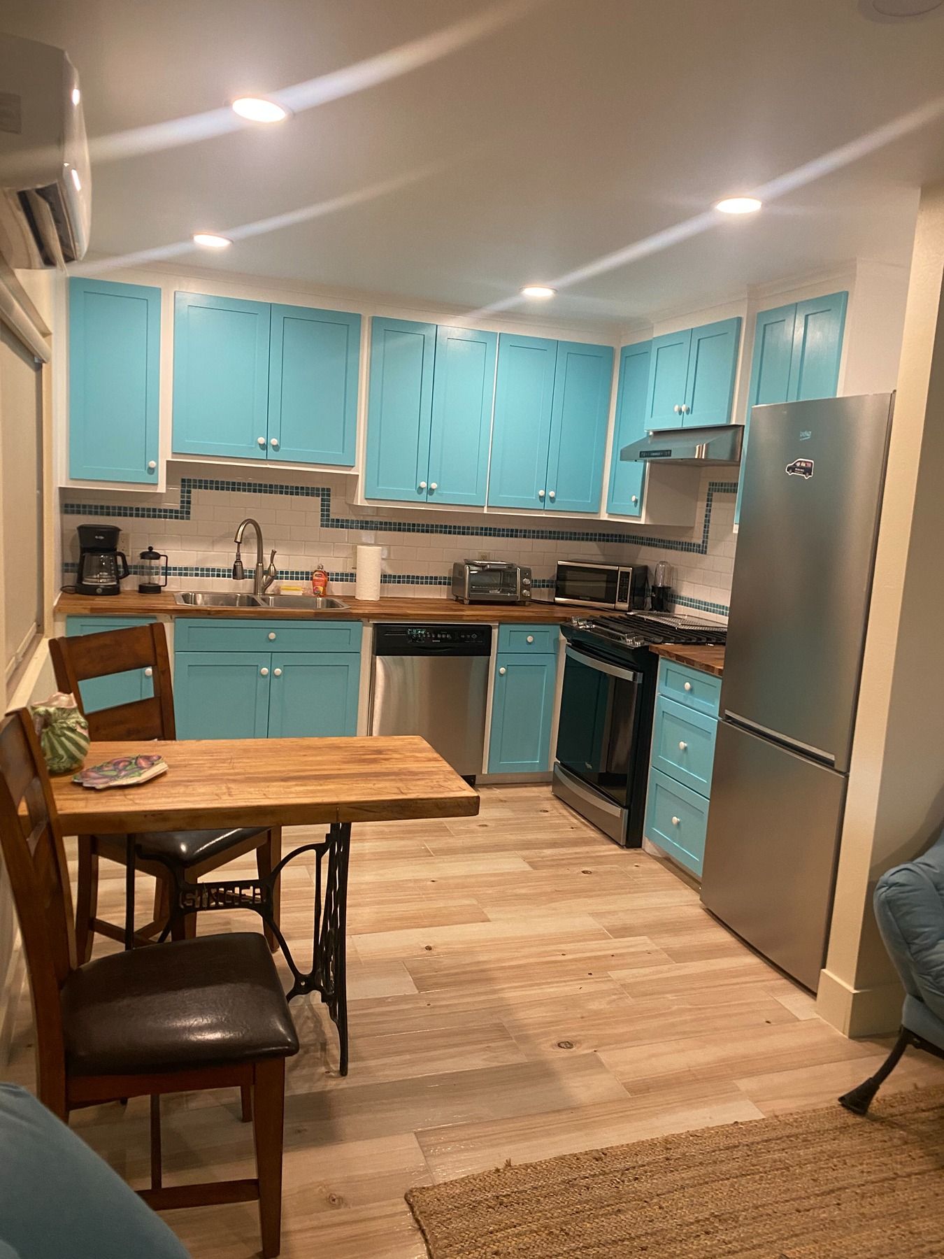 A kitchen with bright blue cabinets, a wooden table with chairs, stainless steel appliances, and light wood flooring.