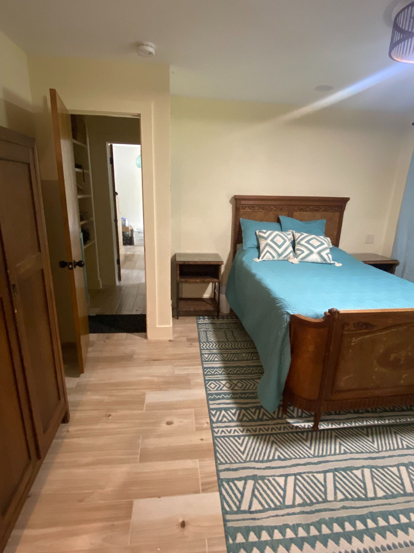 A bedroom with a wooden bed frame, turquoise bedding, patterned rug, light wood flooring, and an open doorway to a closet.