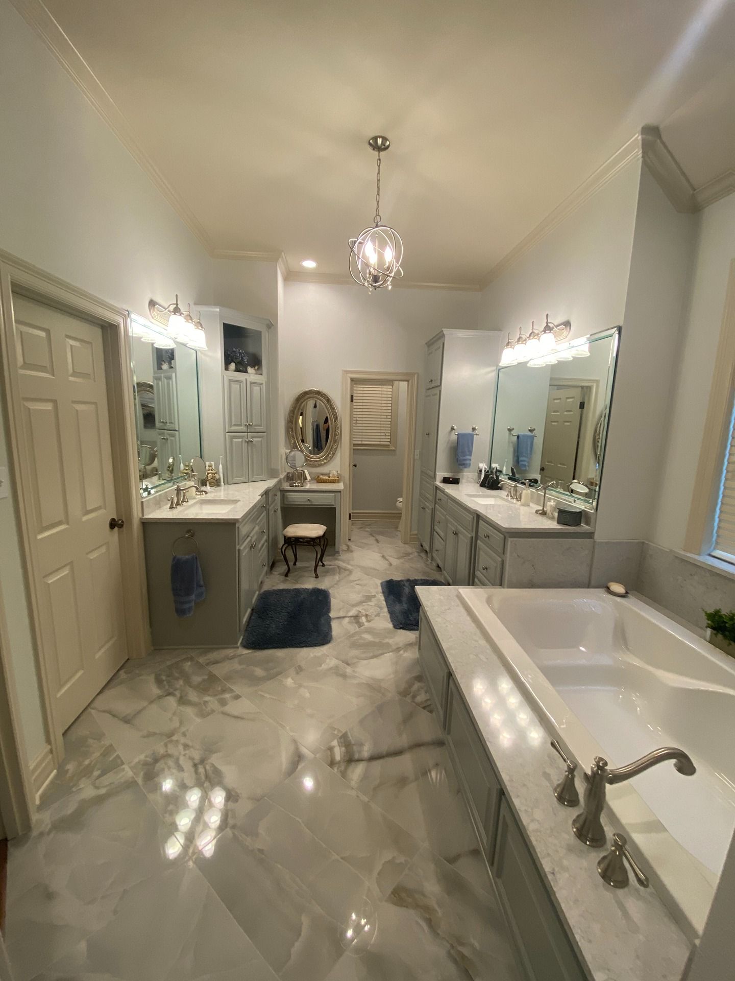 A spacious, luxury bathroom with marble flooring, double vanities, a central makeup area, and a built-in soaking tub.