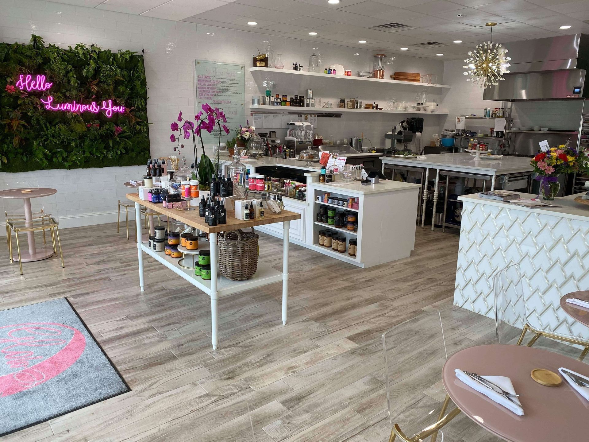 A brightly lit cafe interior featuring a neon sign, a display table with merchandise, and light wood-look flooring.