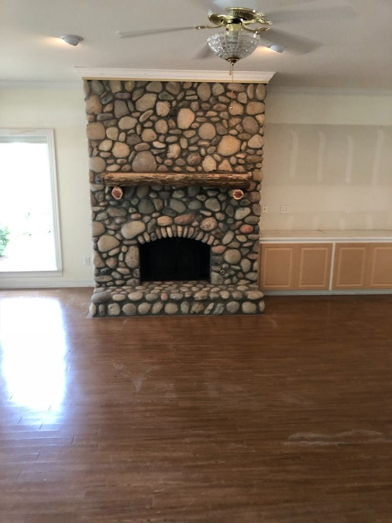 A fireplace with a rustic stone surround and a natural wood mantel, set in a room with hardwood floors.