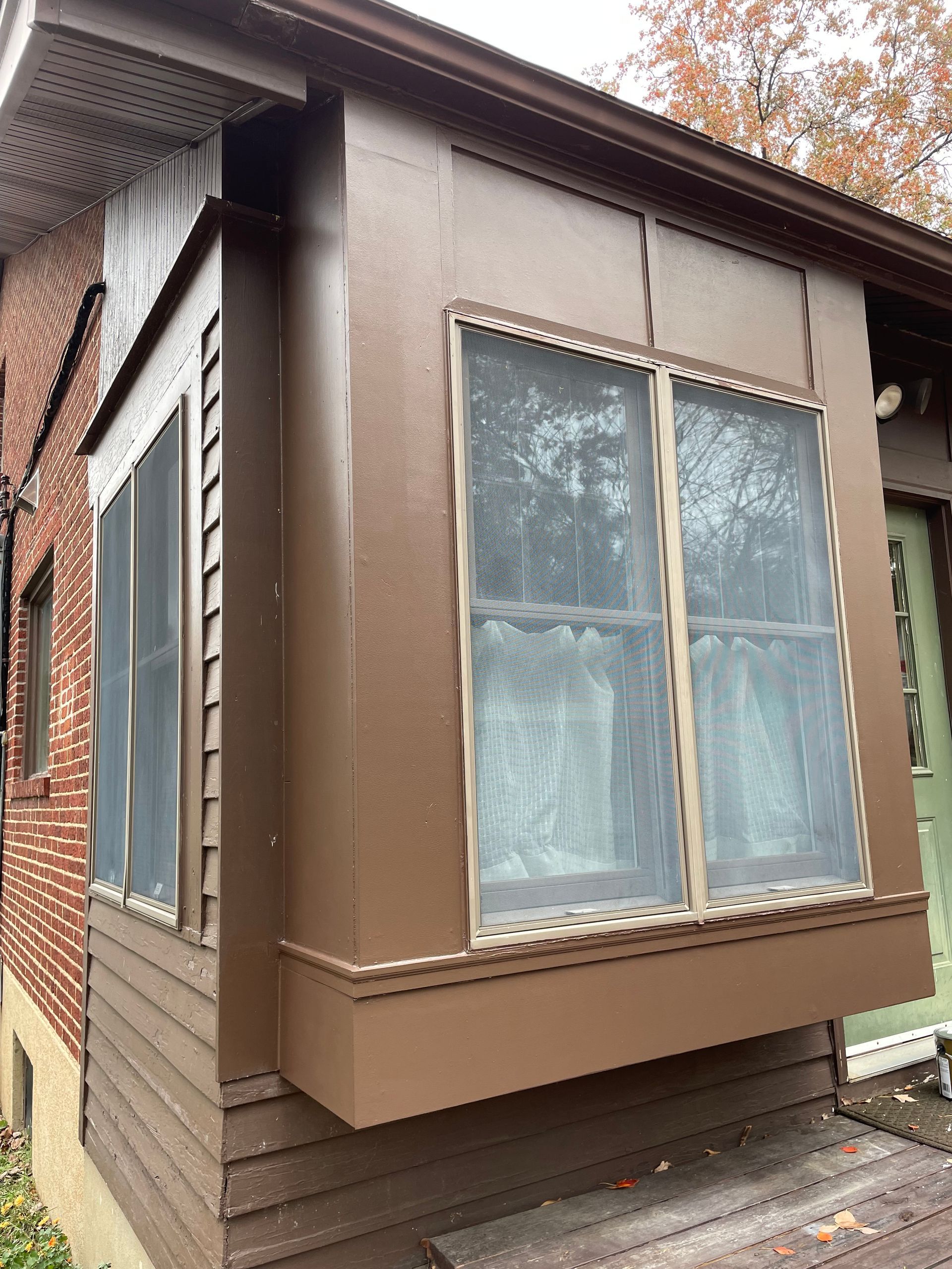 Brown-painted exterior of a house with a window box and two screened windows.