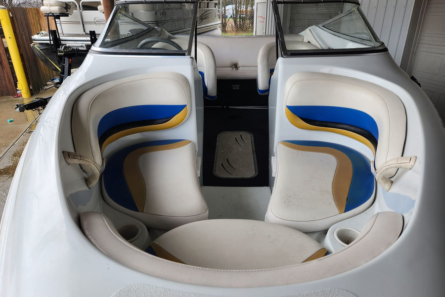 A white boat’s bow seating area with beige, blue, and yellow upholstered cushions and dual windshields.