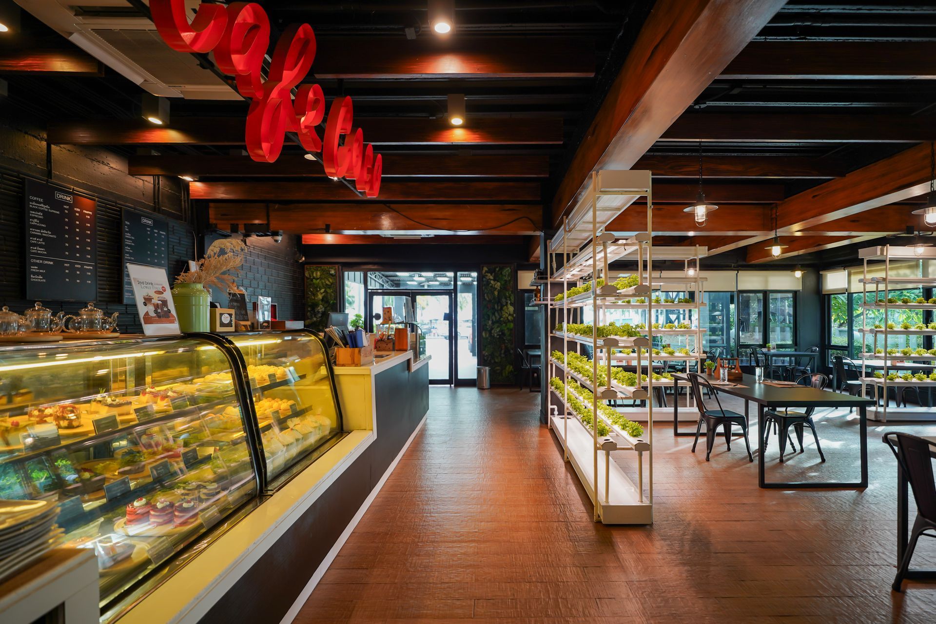 ภาพภายในร้านกาแฟที่มีตู้โชว์ขนมอบ พื้นที่นั่งเล่น และชั้นวางต้นไม้