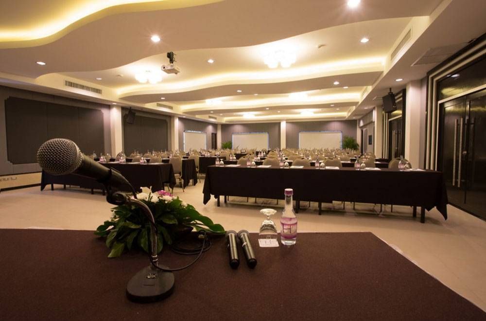 ห้องประชุมถูกจัดเตรียมสำหรับการประชุม โดยมีไมโครโฟนวางอยู่บนโต๊ะ โต๊ะและเก้าอี้เรียงเป็นแถว และจอฉายภาพ