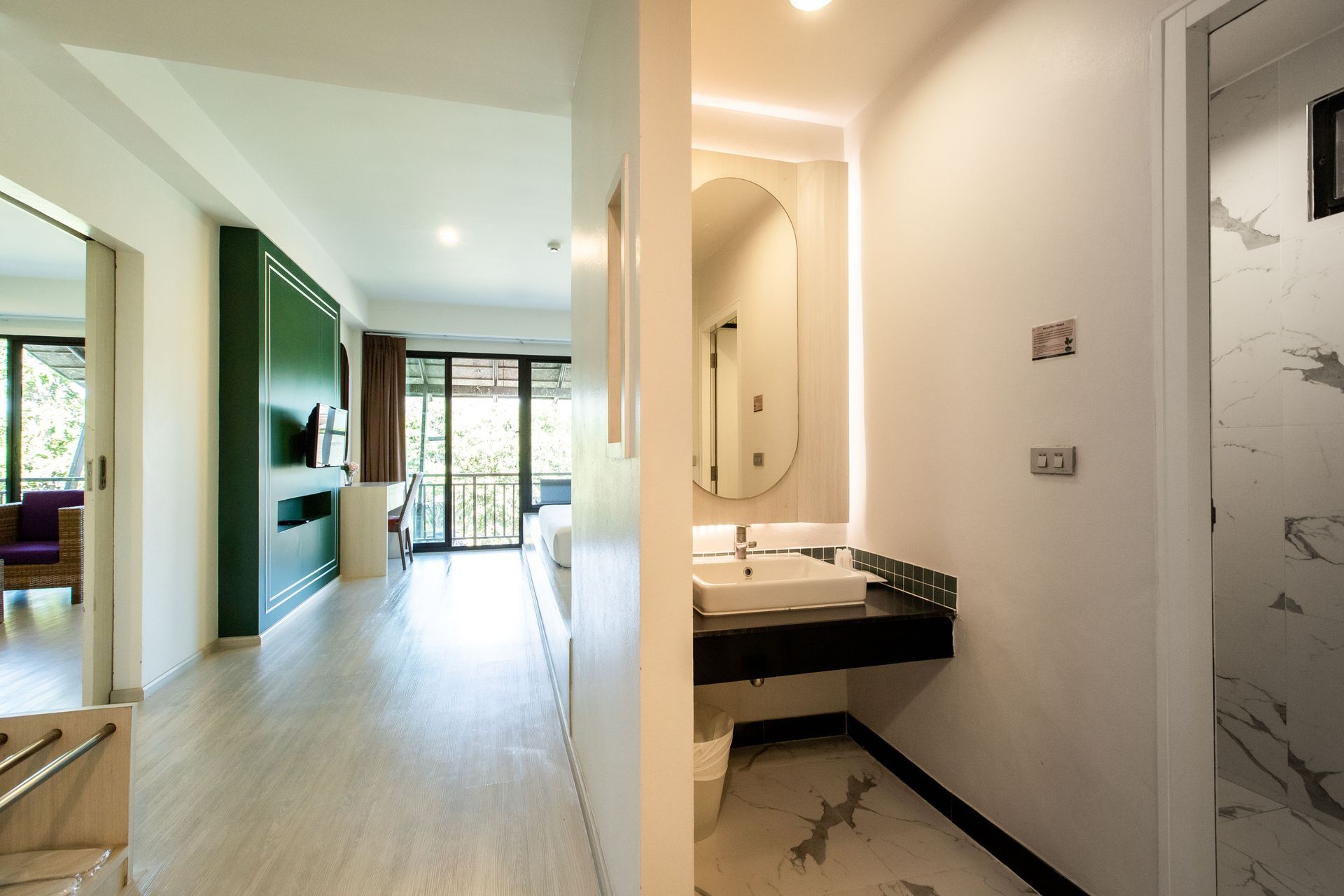 ทางเดินห้องพักโรงแรม มีห้องน้ำ อ่างล้างหน้า และประตูเปิดออกสู่ระเบียงที่มีเตียงนอน