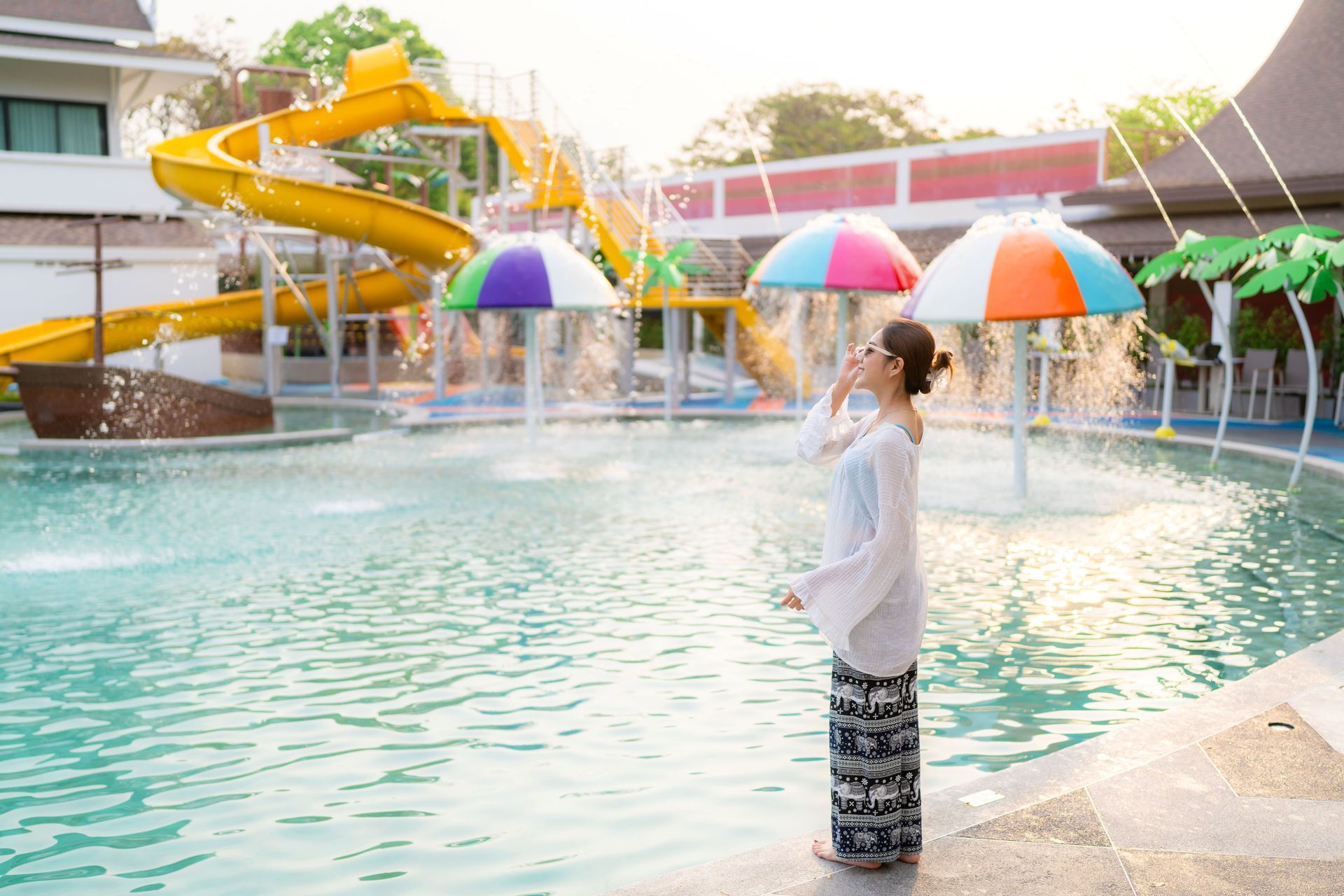 หญิงสาวคนหนึ่งยืนอยู่ใกล้สระน้ำ หันหน้าไปทางน้ำพุ โดยมีสไลเดอร์น้ำอยู่ด้านหลัง