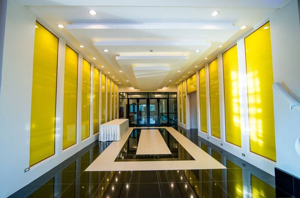 ทางเดินยาวที่มีแผ่นผนังสีเหลือง พื้นปูด้วยสีดำสลับขาว และมีโต๊ะอยู่ใกล้ทางเข้า