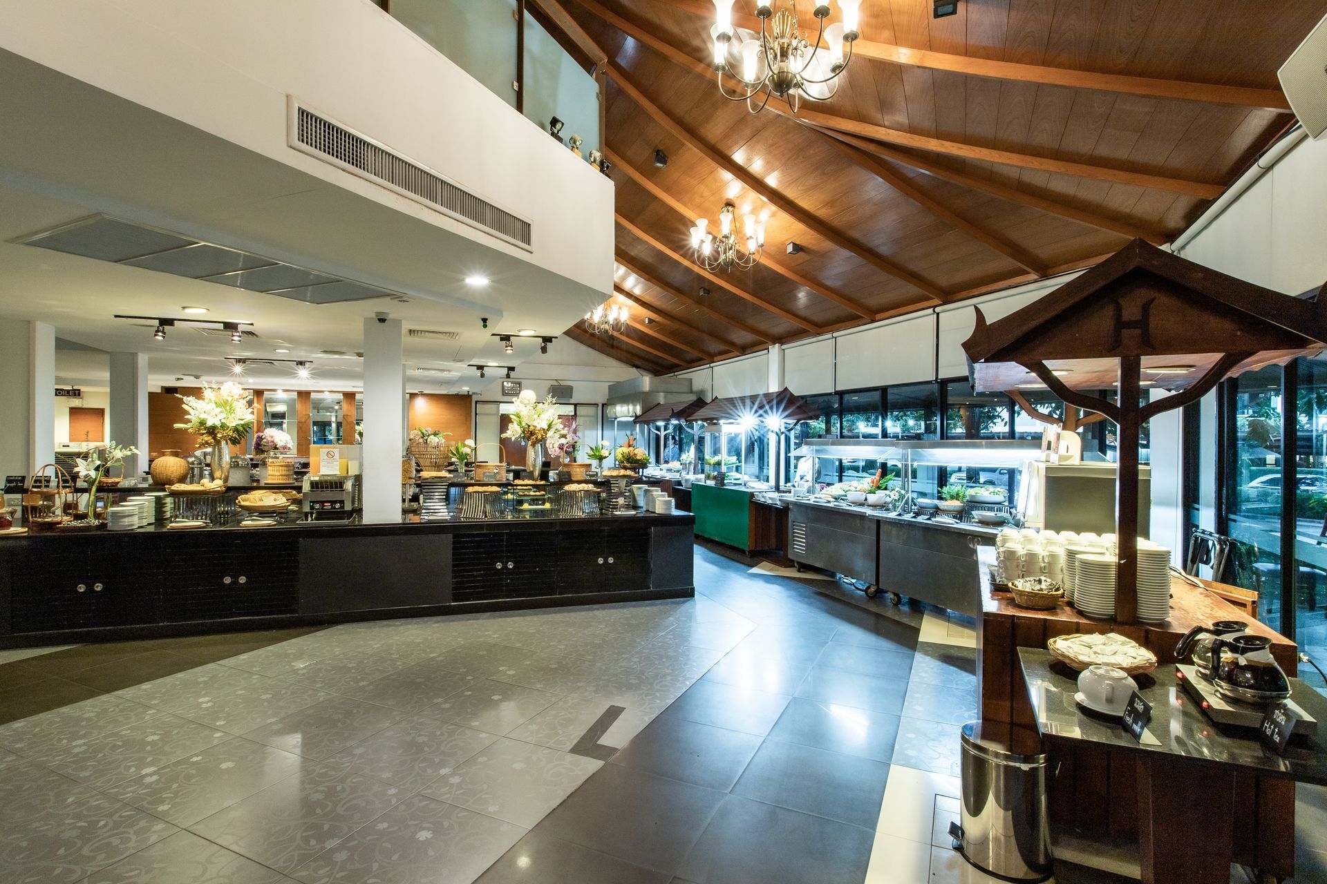 บริเวณบุฟเฟต์ในร้านอาหารที่มีโต๊ะสำหรับเสิร์ฟอาหาร เพดานไม้ และโคมระย้า