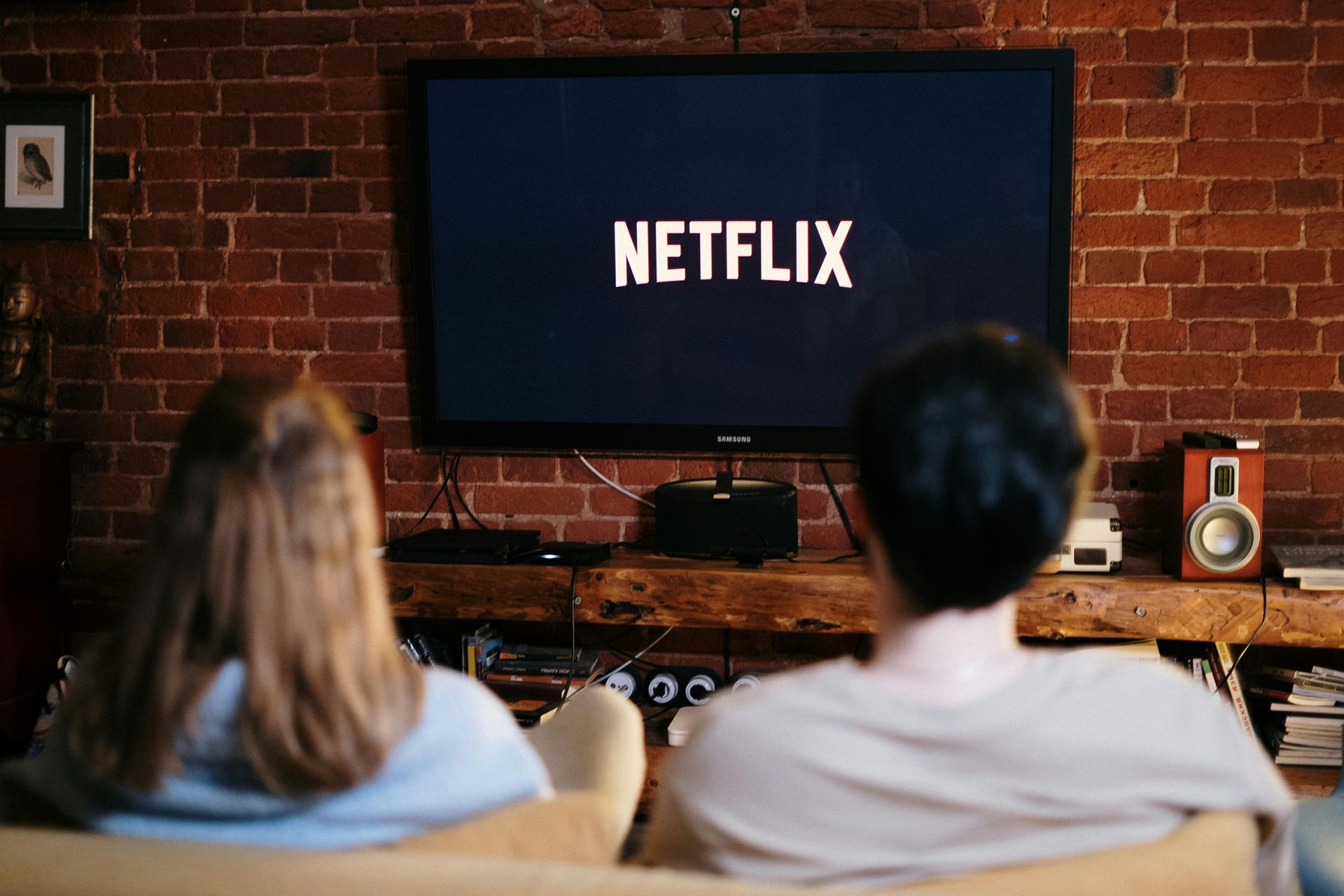 Two people watching Netflix on a large TV in a room with a brick wall.