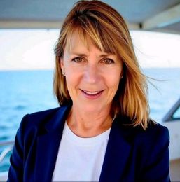 Smiling woman in a blue blazer and white shirt on a boat with the ocean behind her