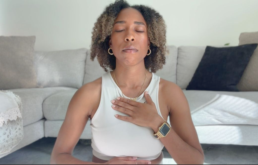 Person meditating on a couch, hand on chest, eyes closed.