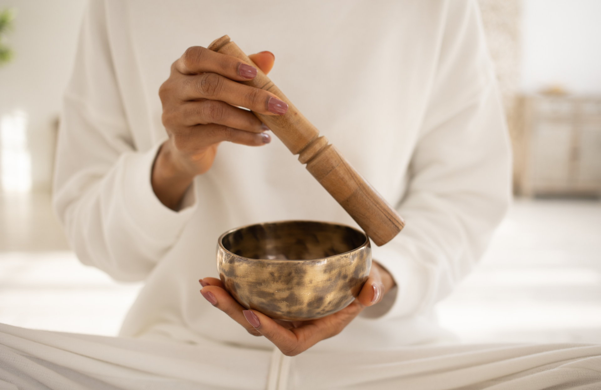 Person in white clothing holding a singing bowl and mallet during meditation