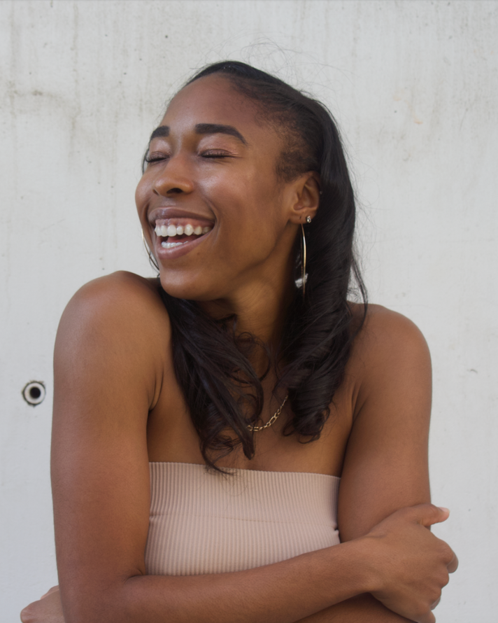 Smiling person with crossed arms, laughing against a light wall