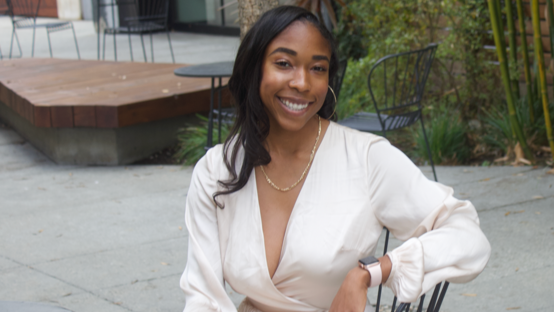 Smiling woman in a white blouse seated outdoors on a patio bench