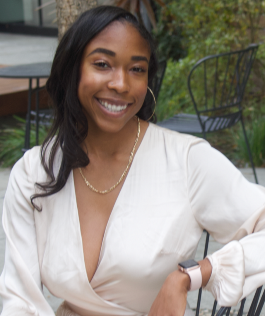 Smiling woman in a white blouse sitting outdoors on a patio.