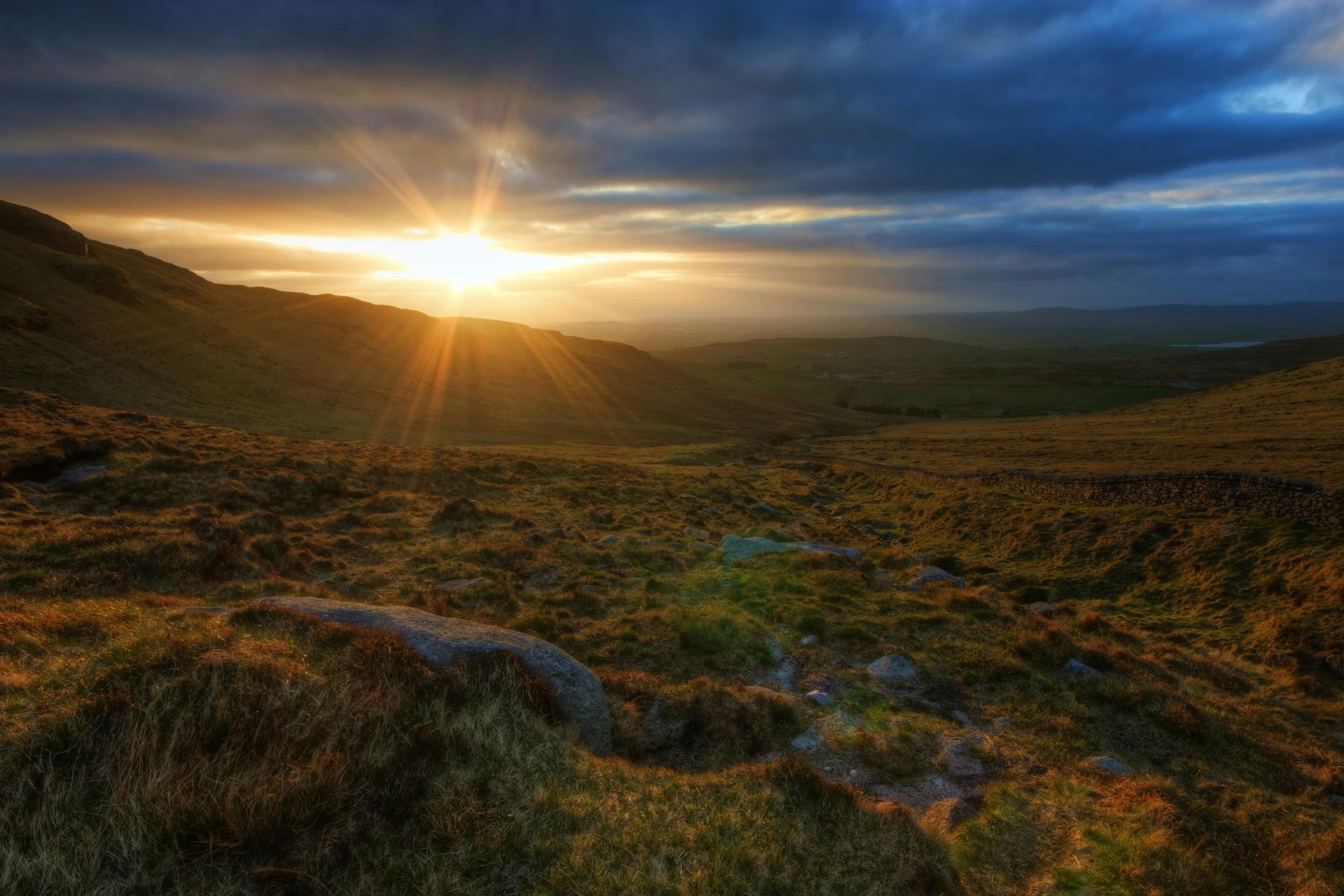 Sunrise over a grassy mountain landscape with dramatic clouds and golden light
