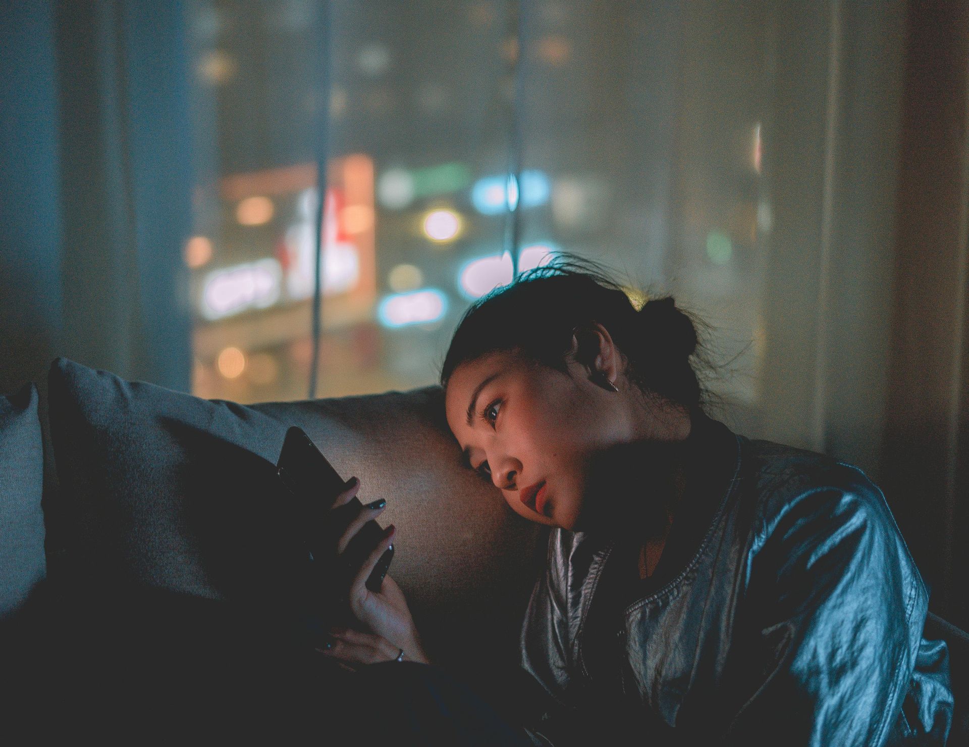 Person leaning toward a cat on a couch in a dimly lit room with blurred city lights in the background