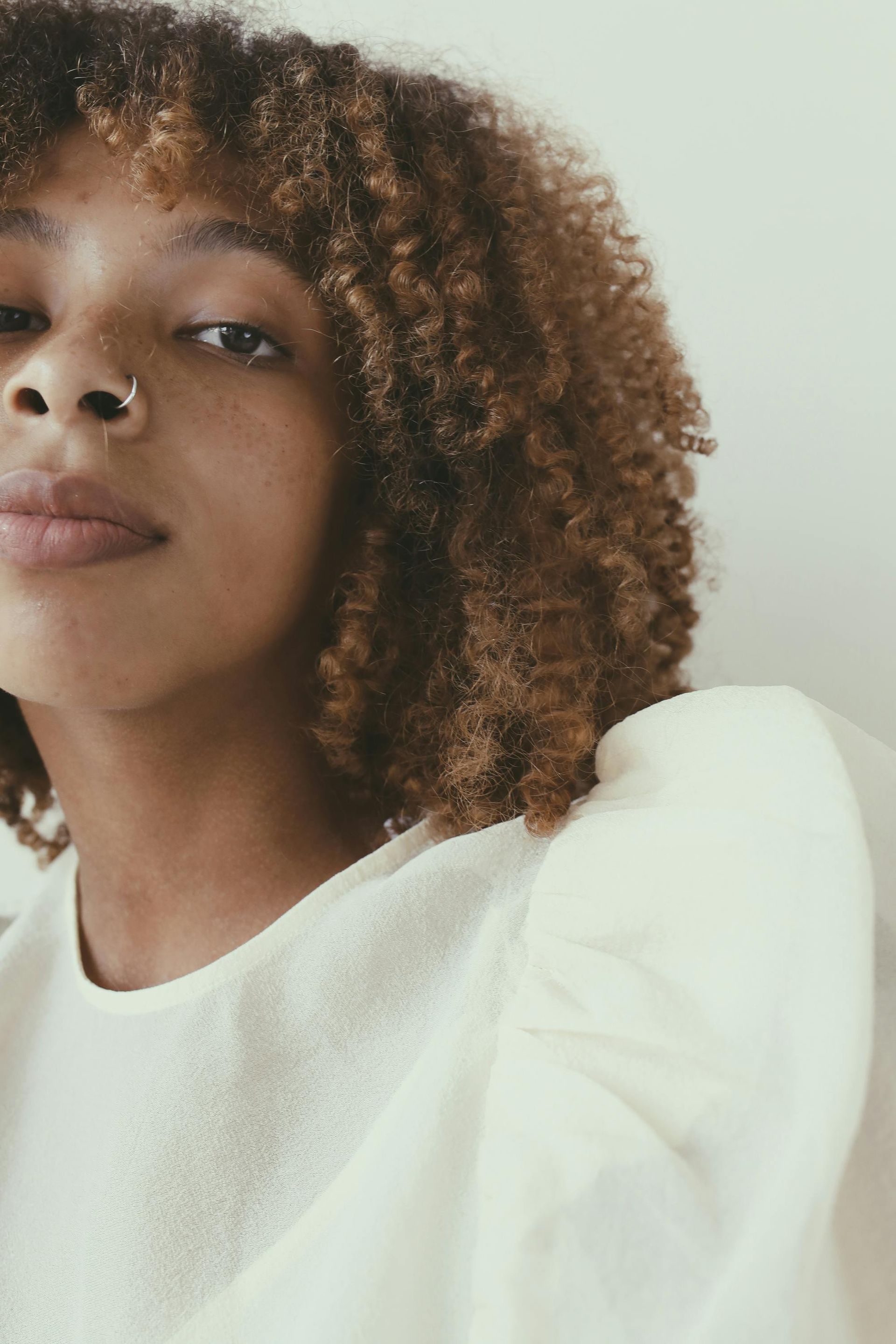 Close-up portrait of a person with curly hair in a white top against a soft light background