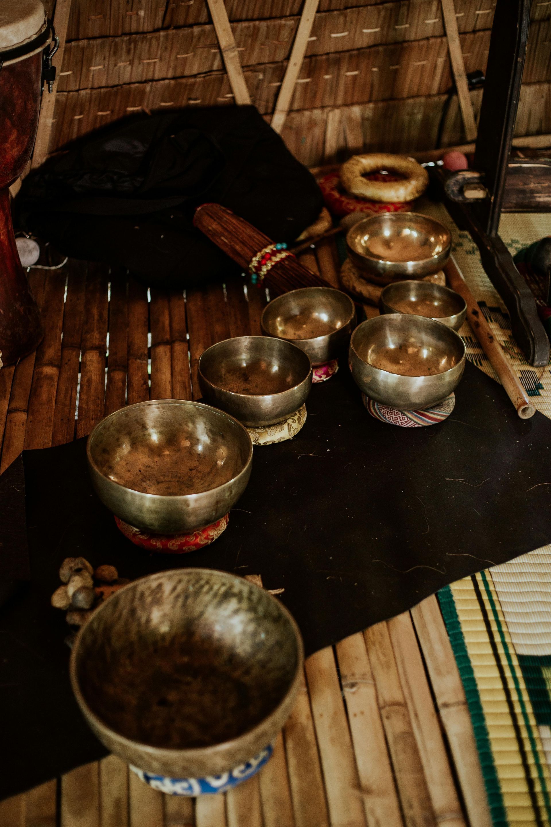 Metal bowls and a pot arranged on a woven mat beside a black cushion in a rustic room